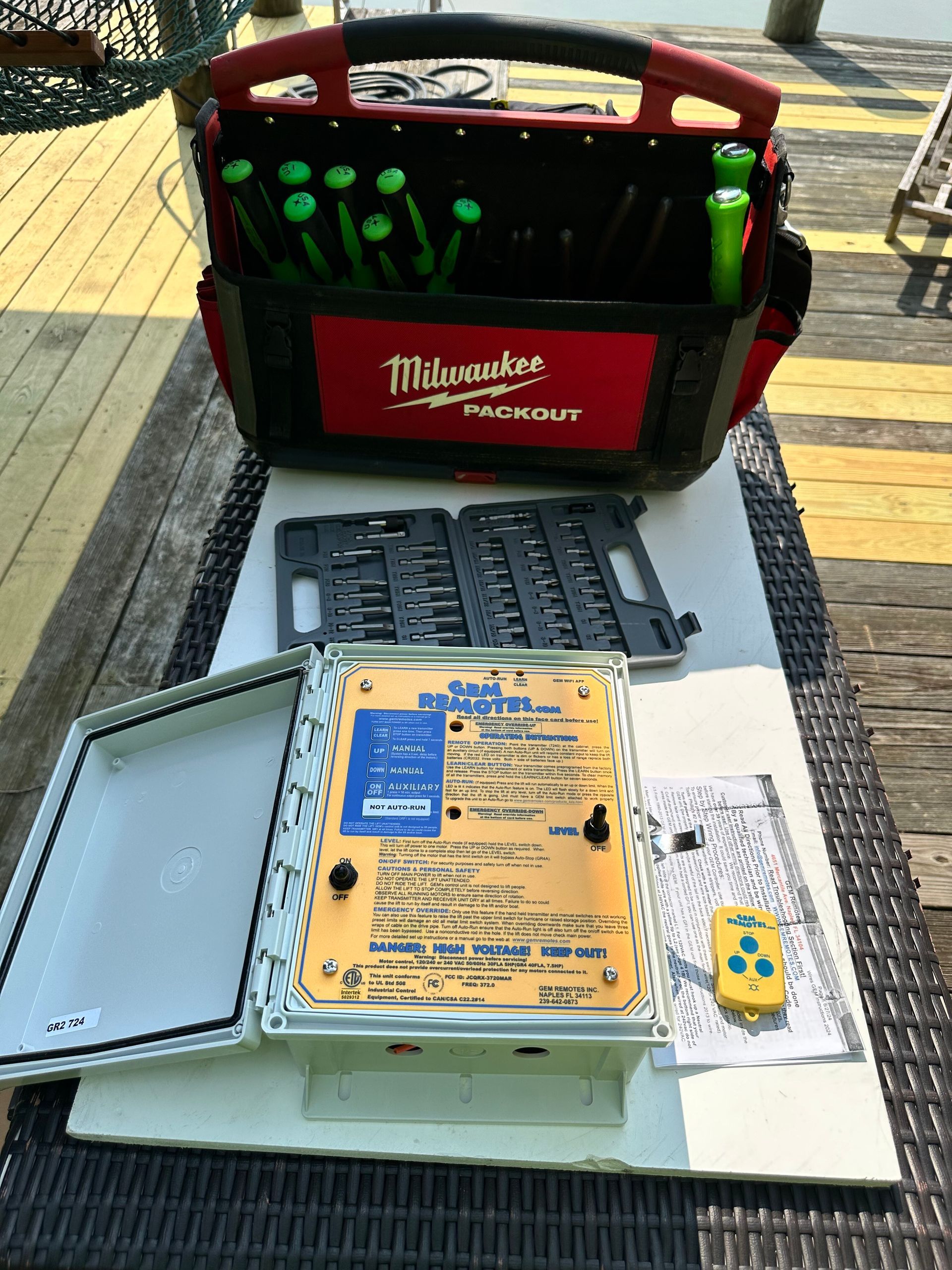 Tool bag, open electrical box, tools, and a control device on a wooden dock.