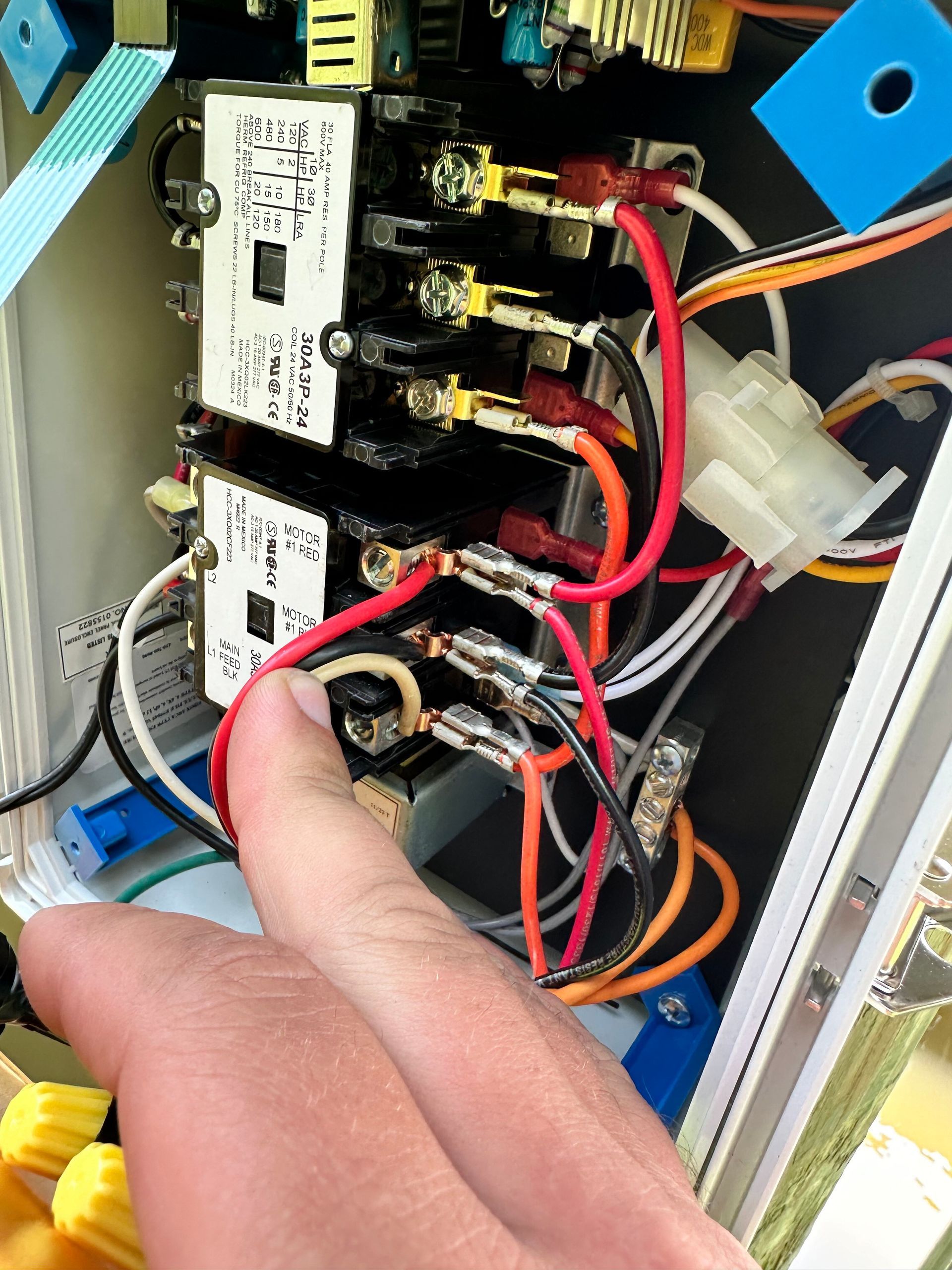 Hand pointing to electrical wiring inside a control box. Red and black wires are prominent.