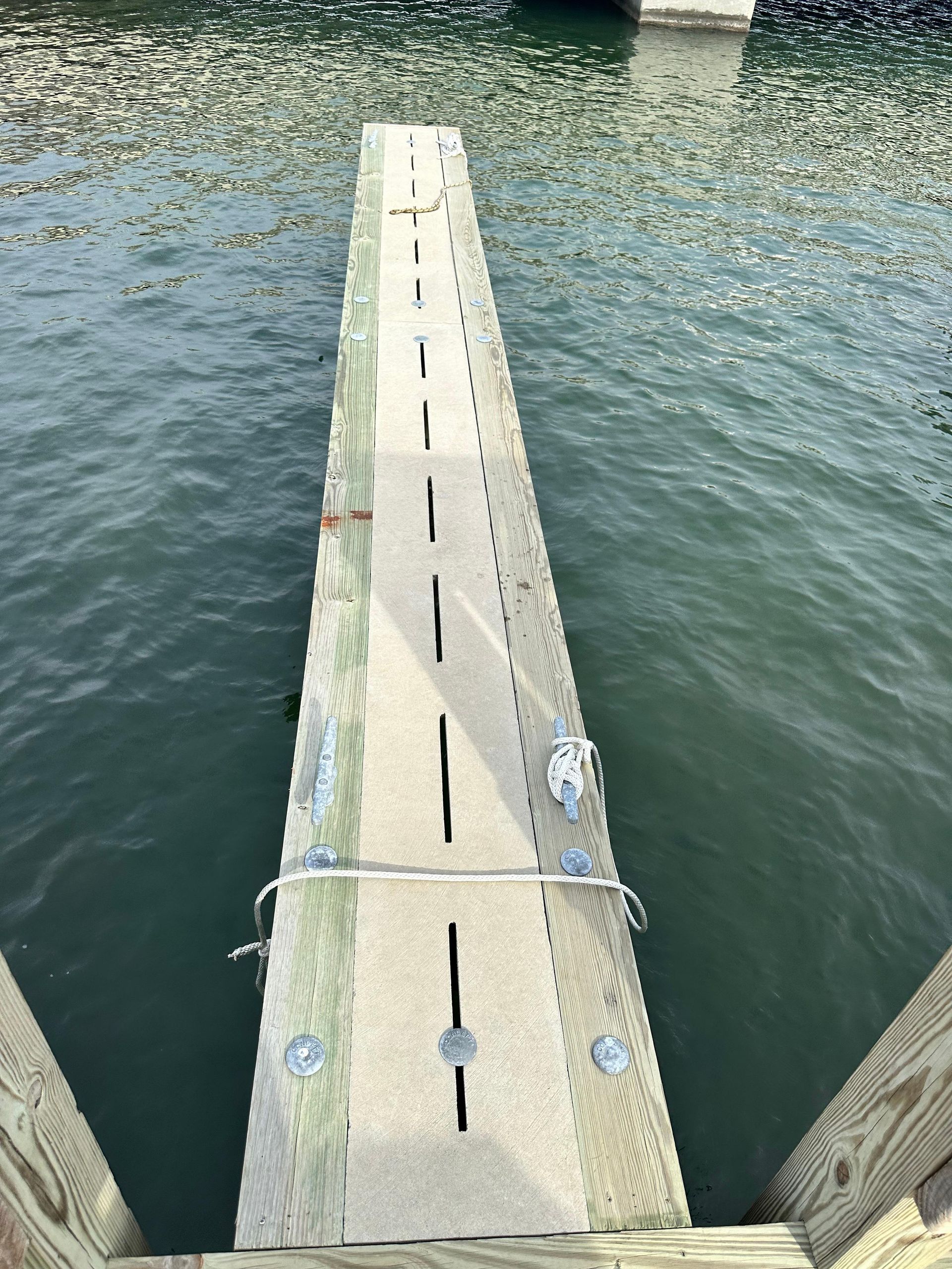 A wooden dock extending into water; includes a handrail and bolt details.