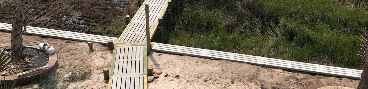 A wooden bridge over a brown area next to green grass.