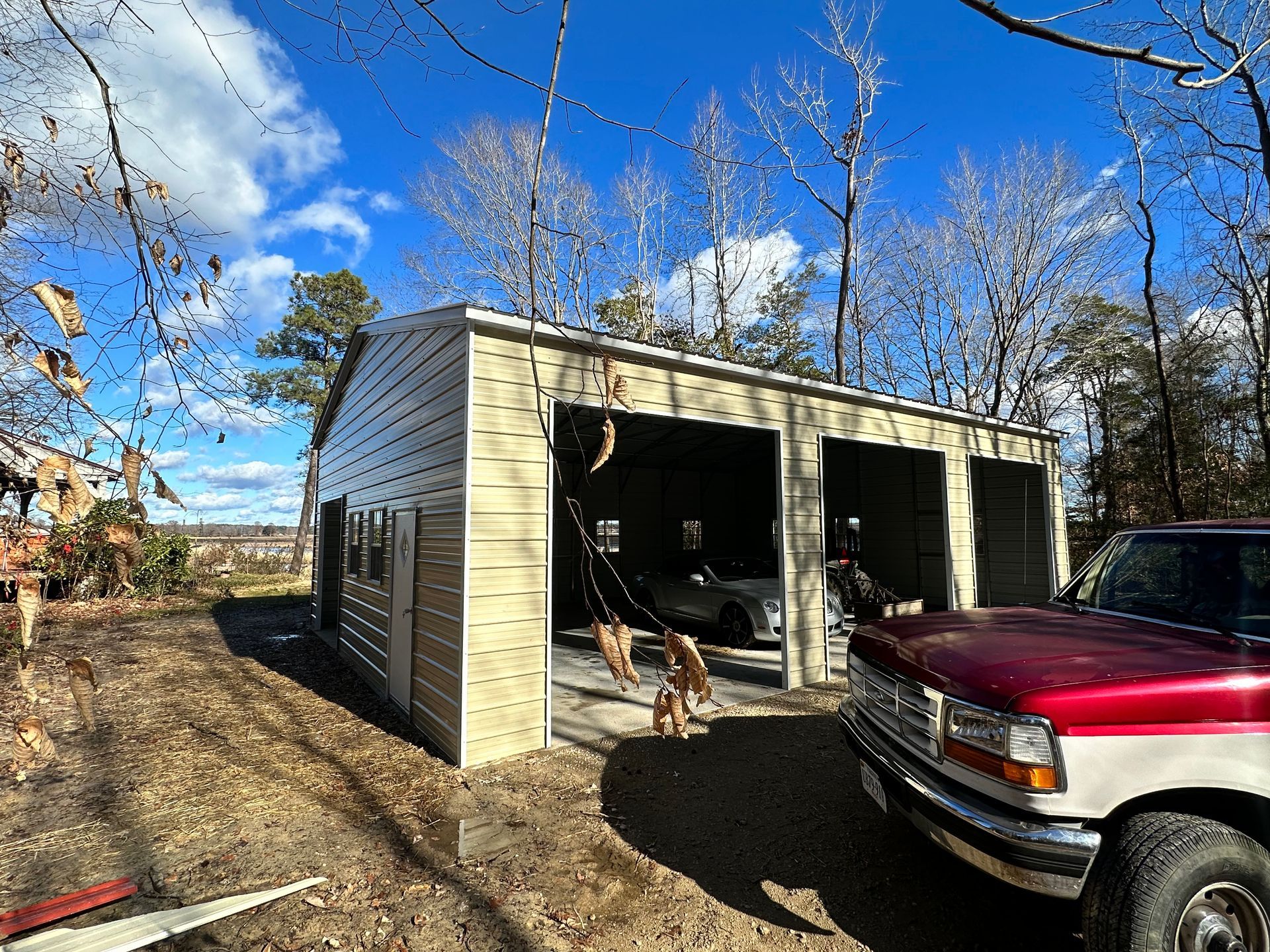 Beige metal garage with open bays. Red and white truck in front. Dogs inside the bay, car visible.