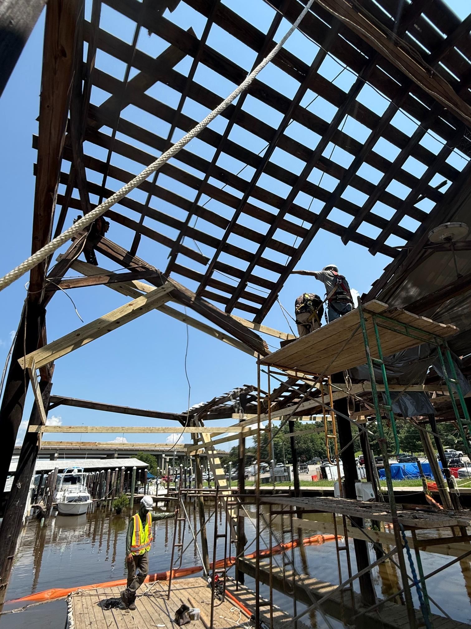 Construction workers repair a boathouse roof over a marina. Bright sky.