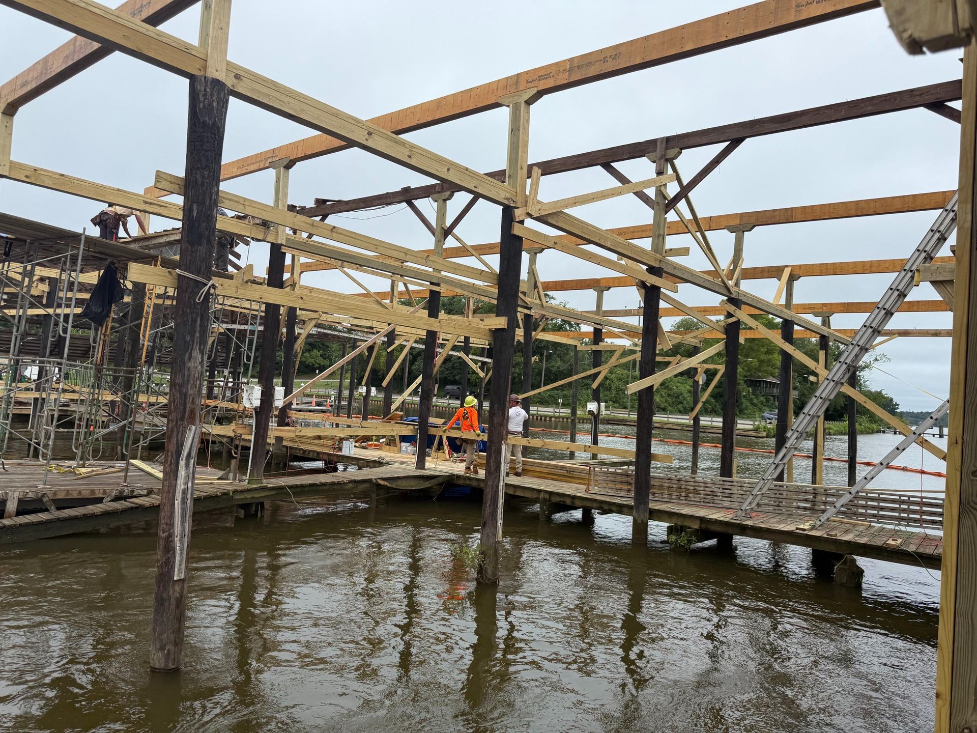 Wooden pier construction over water, workers visible, with cloudy sky.
