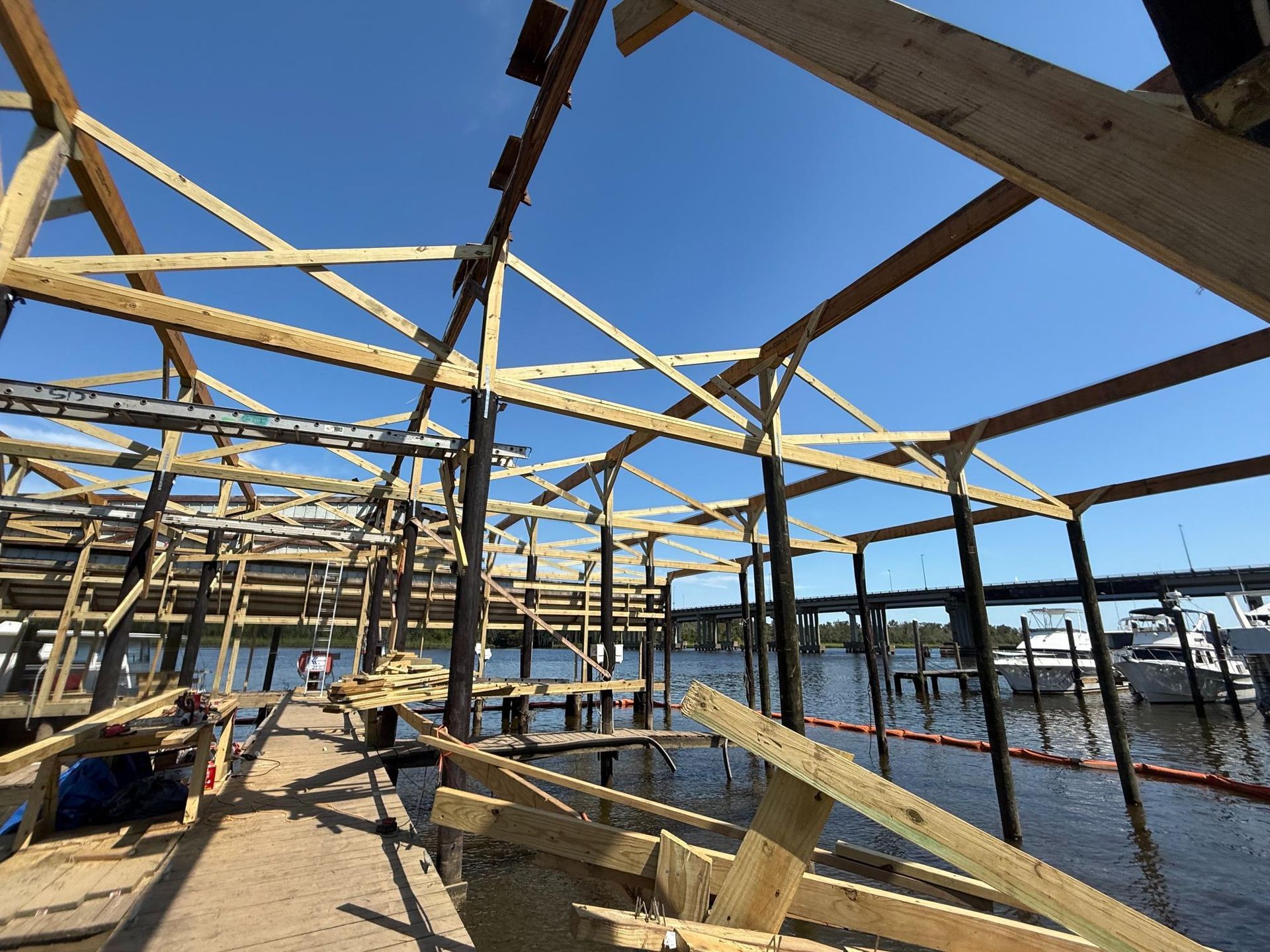 Wooden structure under construction over water, boats and blue sky visible.