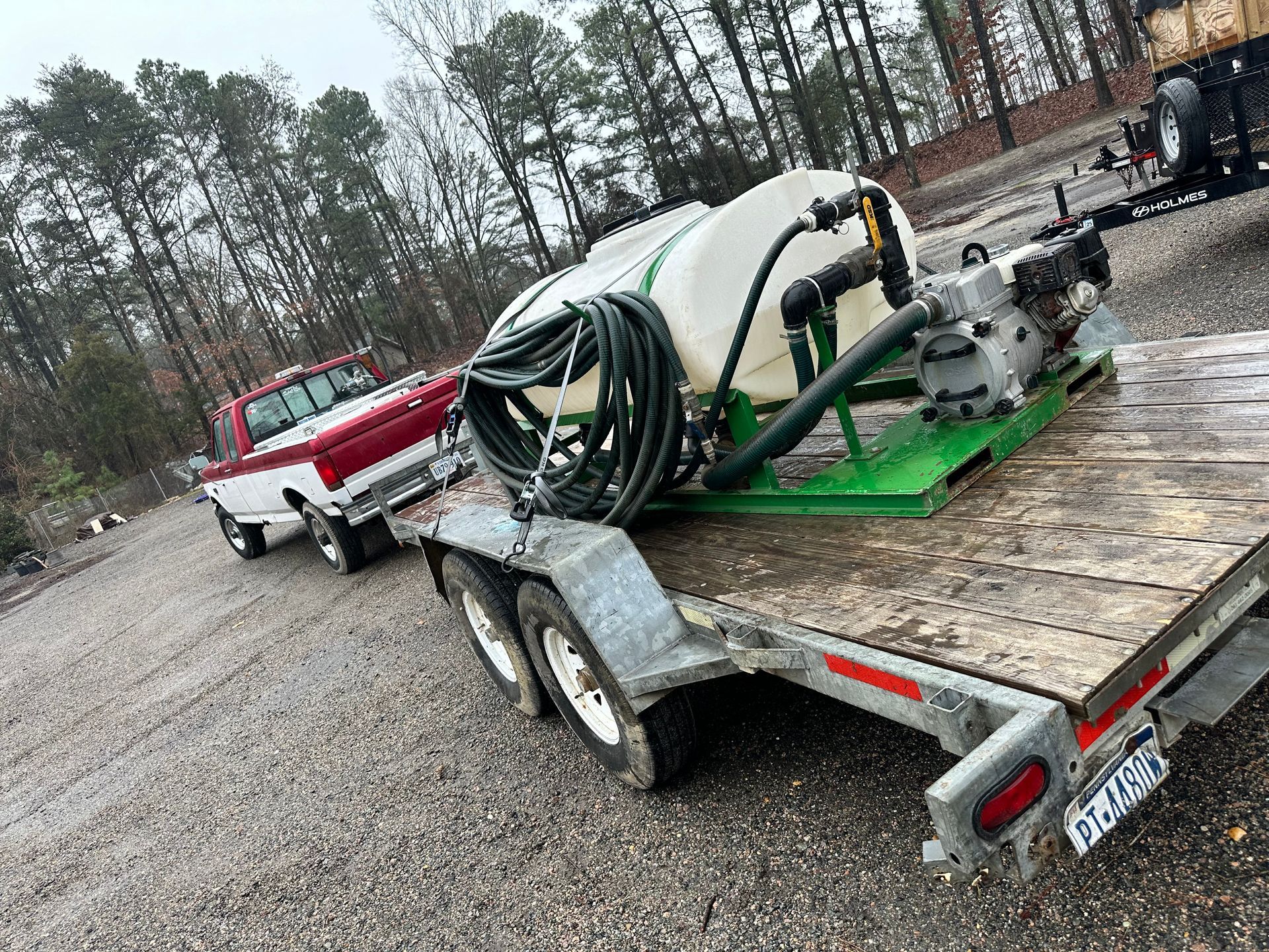 Red and white pickup truck towing a trailer with a white tank and spraying equipment, outdoors.