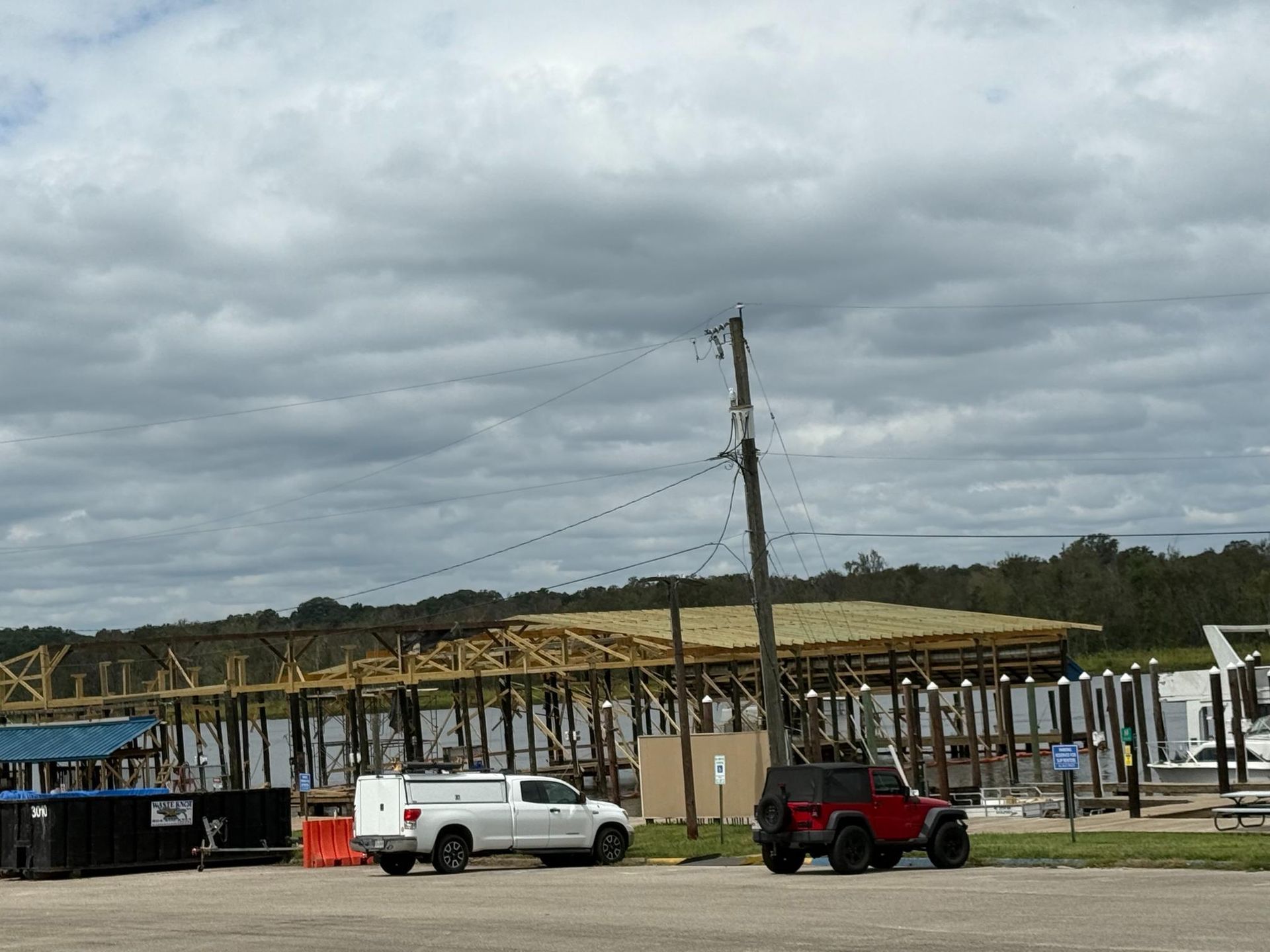A white truck and red Jeep parked near a waterfront pier under cloudy skies.