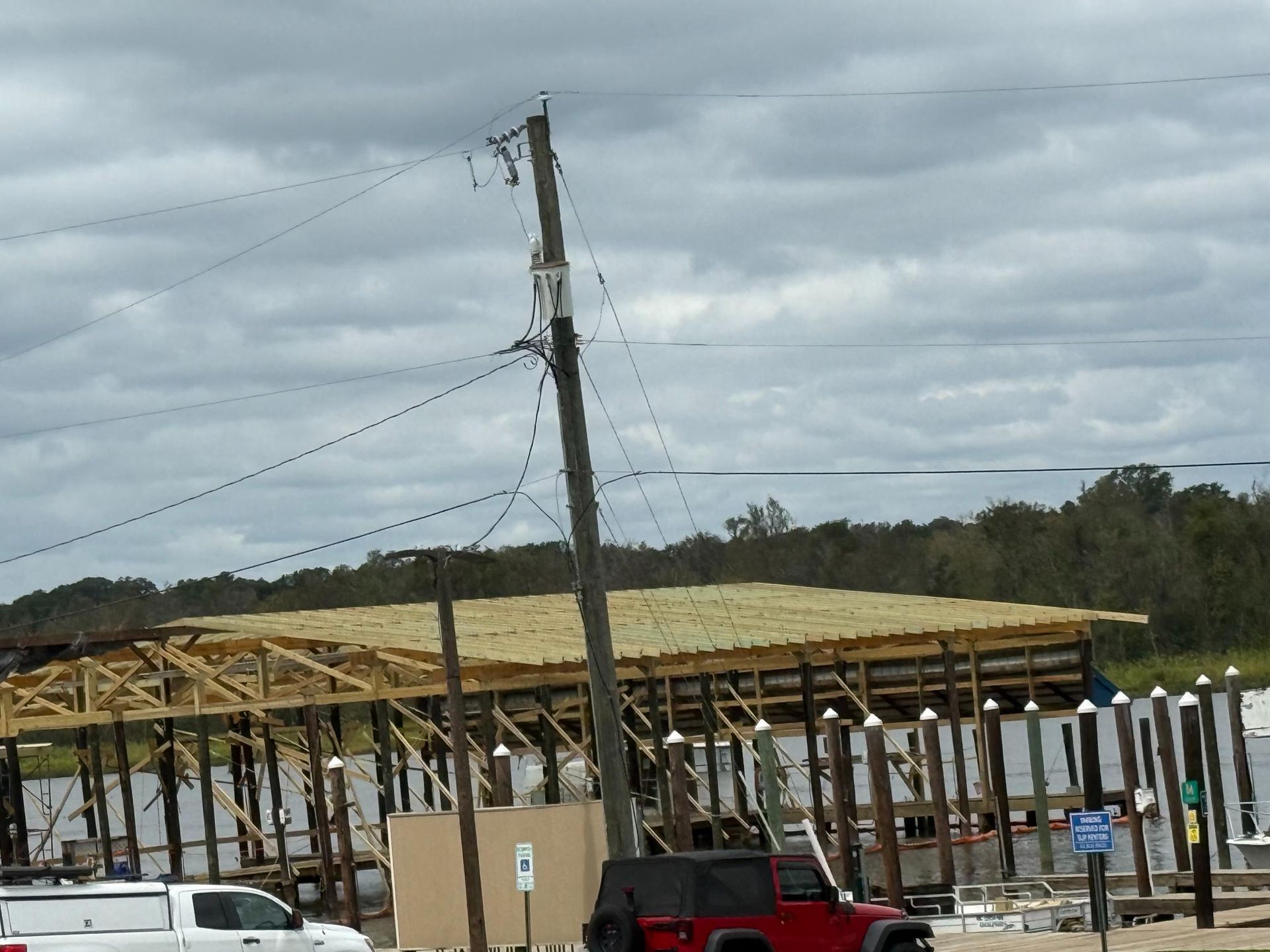 Power pole leaning over a wooden structure under construction, near water, with a cloudy sky.