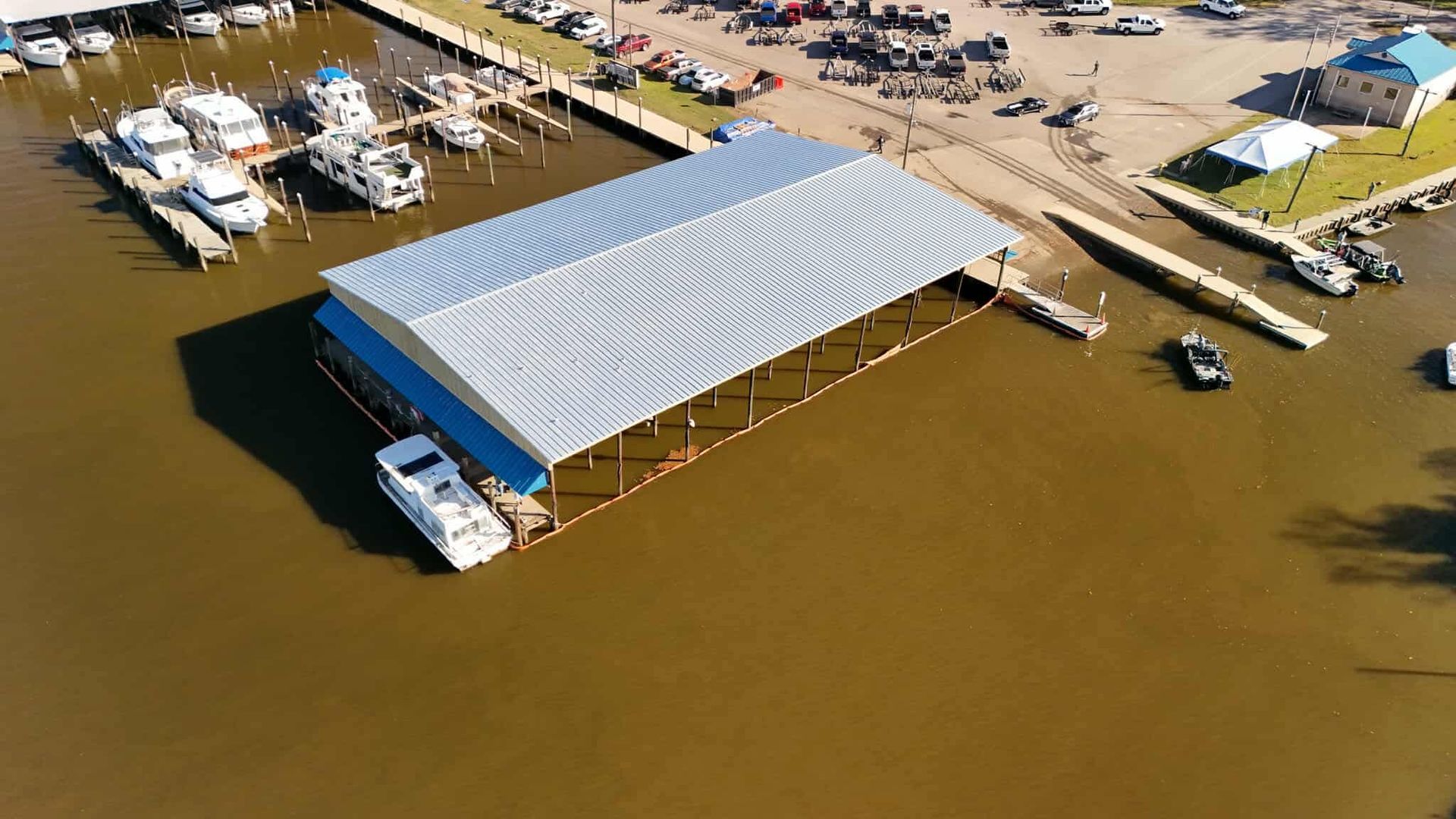 Aerial view of a boat dock with boats, a covered slip, and a parking area near a body of water.
