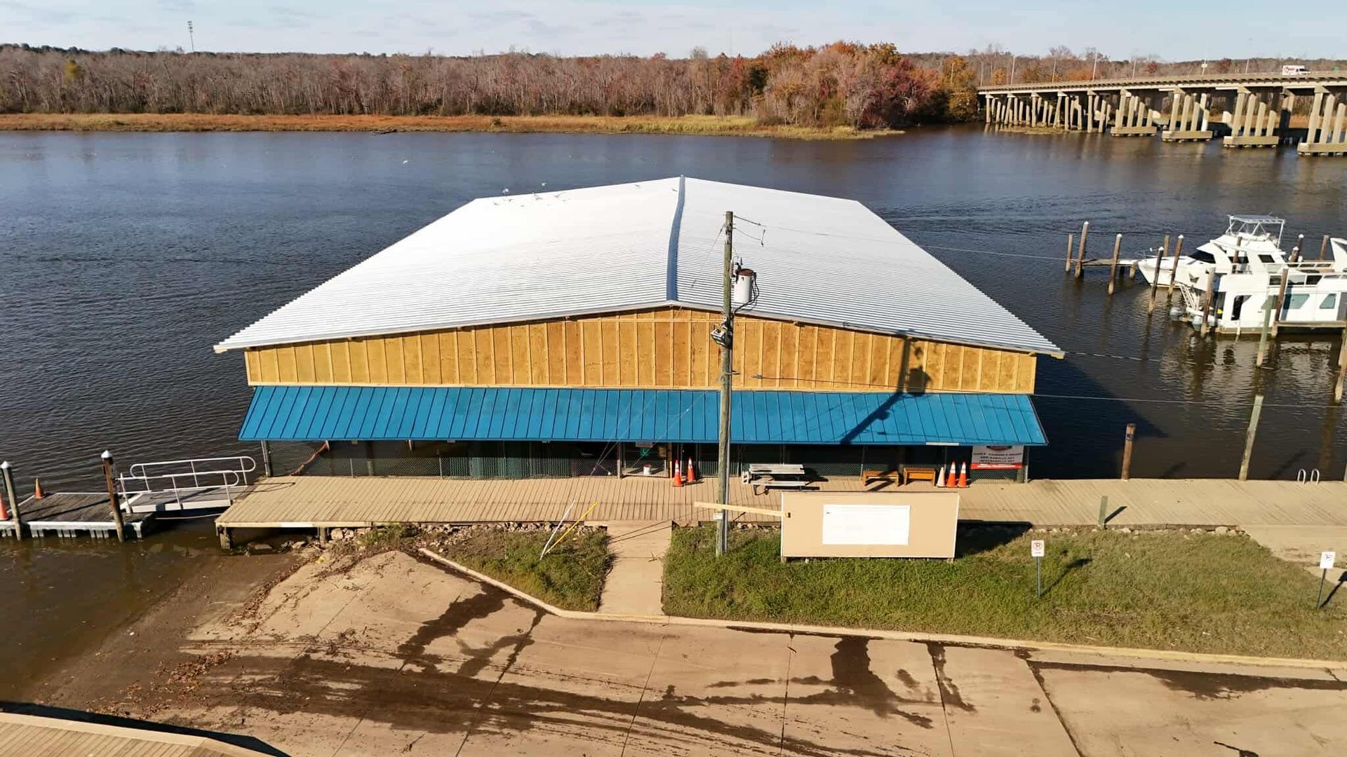 Boathouse with blue trim and metal roof on a lake, with docks and boats visible.