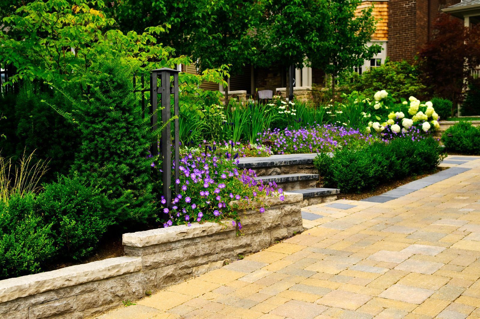 Landscaped garden with stone steps, flowers, and greenery, next to a paved pathway.