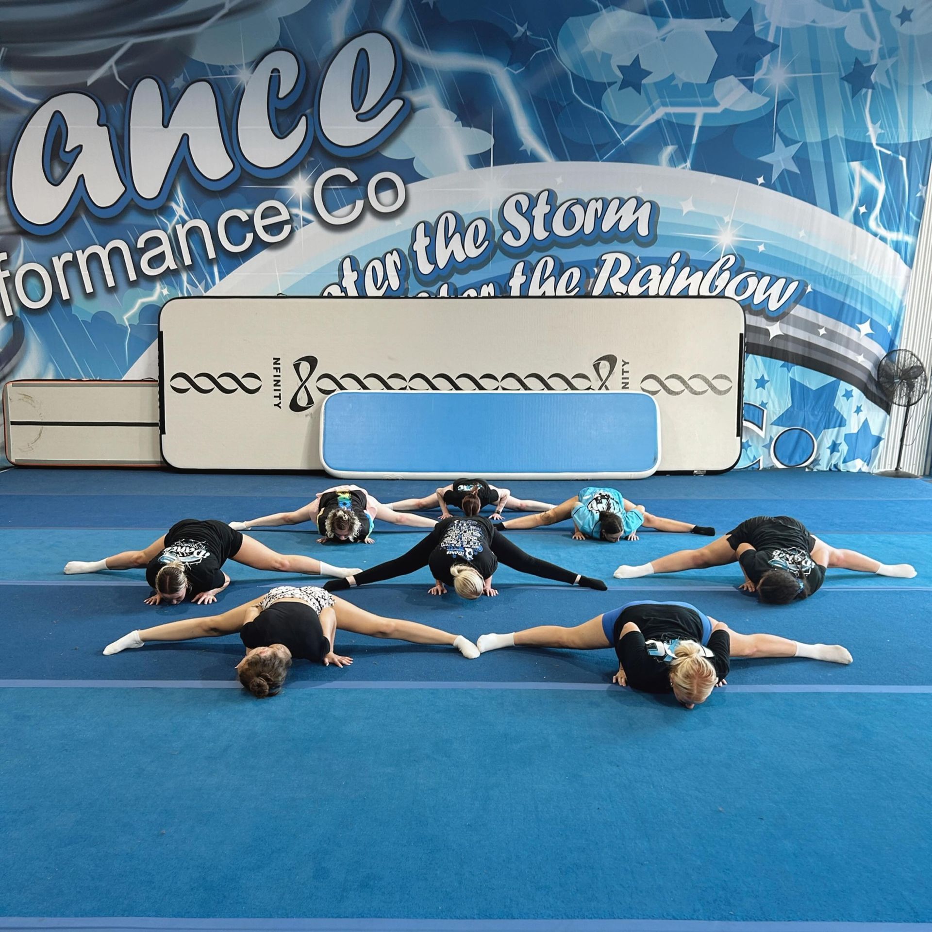 Cheerleaders in a Circle, Performing a Straddle Stretch on a Blue Mat — iDance Performance Co In Medowie, NSW