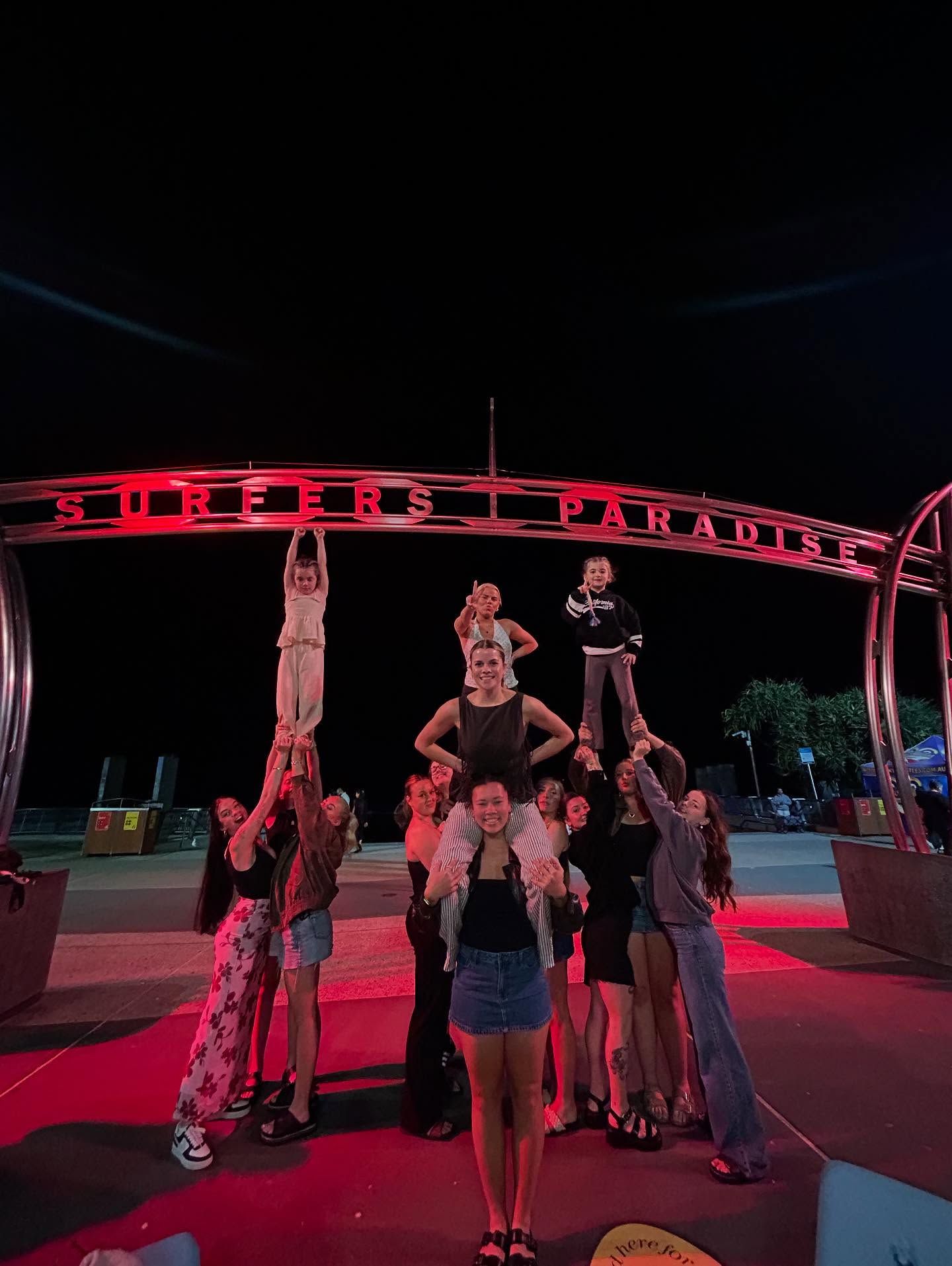 A Group of People Are Doing a Human Pyramid at Night Under a Red-lit Structure — iDance Performance Co In Medowie, NSW