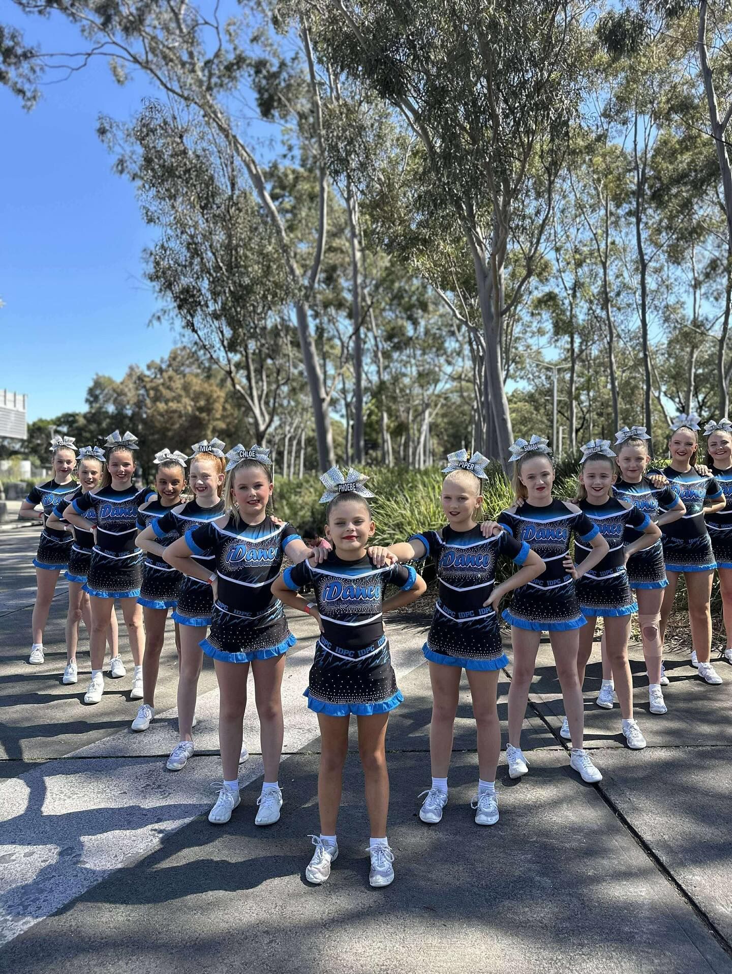 Cheerleaders in Blue and Black Uniforms Pose Outdoors With Arms Outstretched — iDance Performance Co In Medowie, NSW