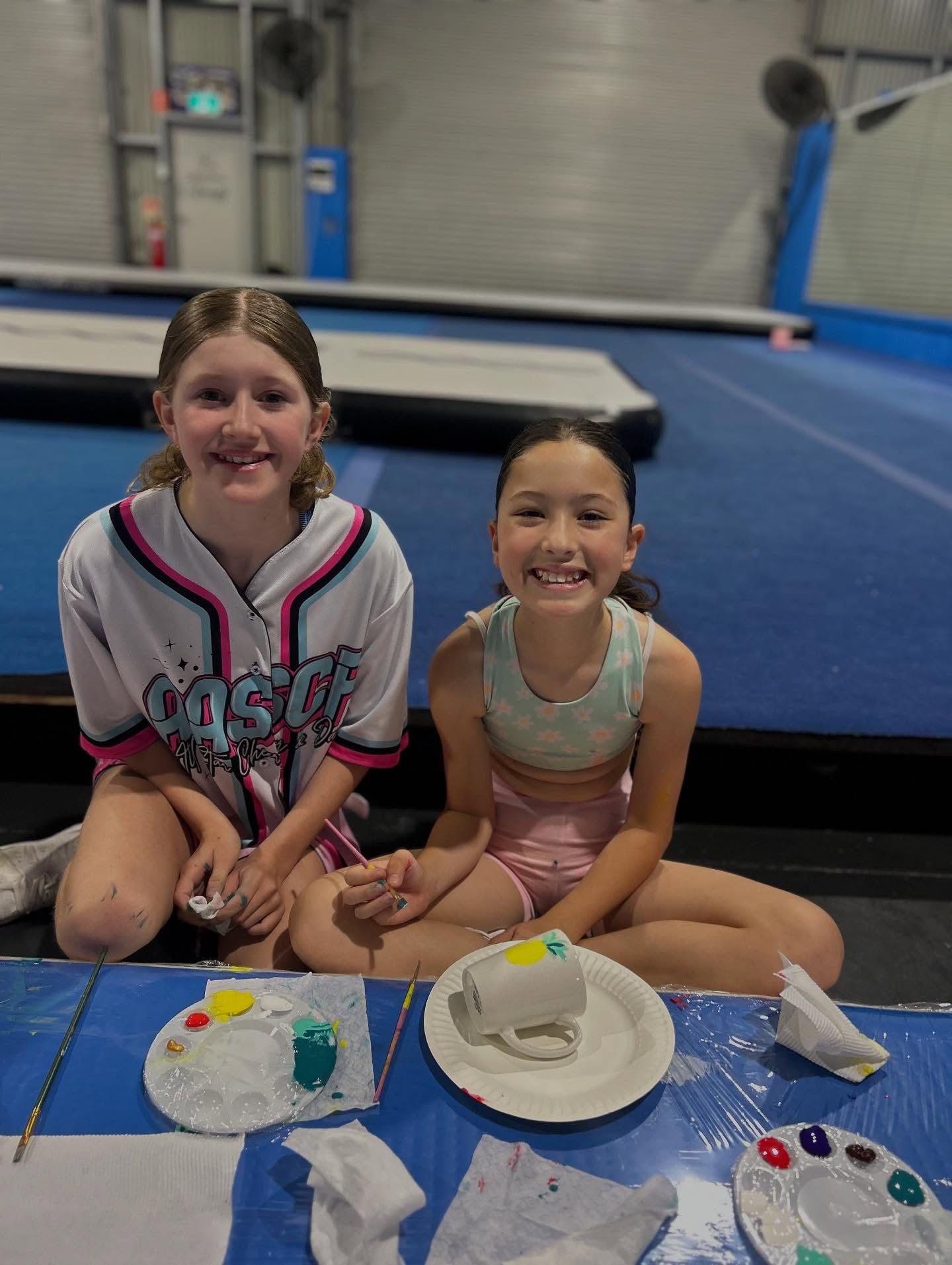 Two Girls Smiling, Painting Pottery on a Blue Mat in a Gym — iDance Performance Co In Medowie, NSW