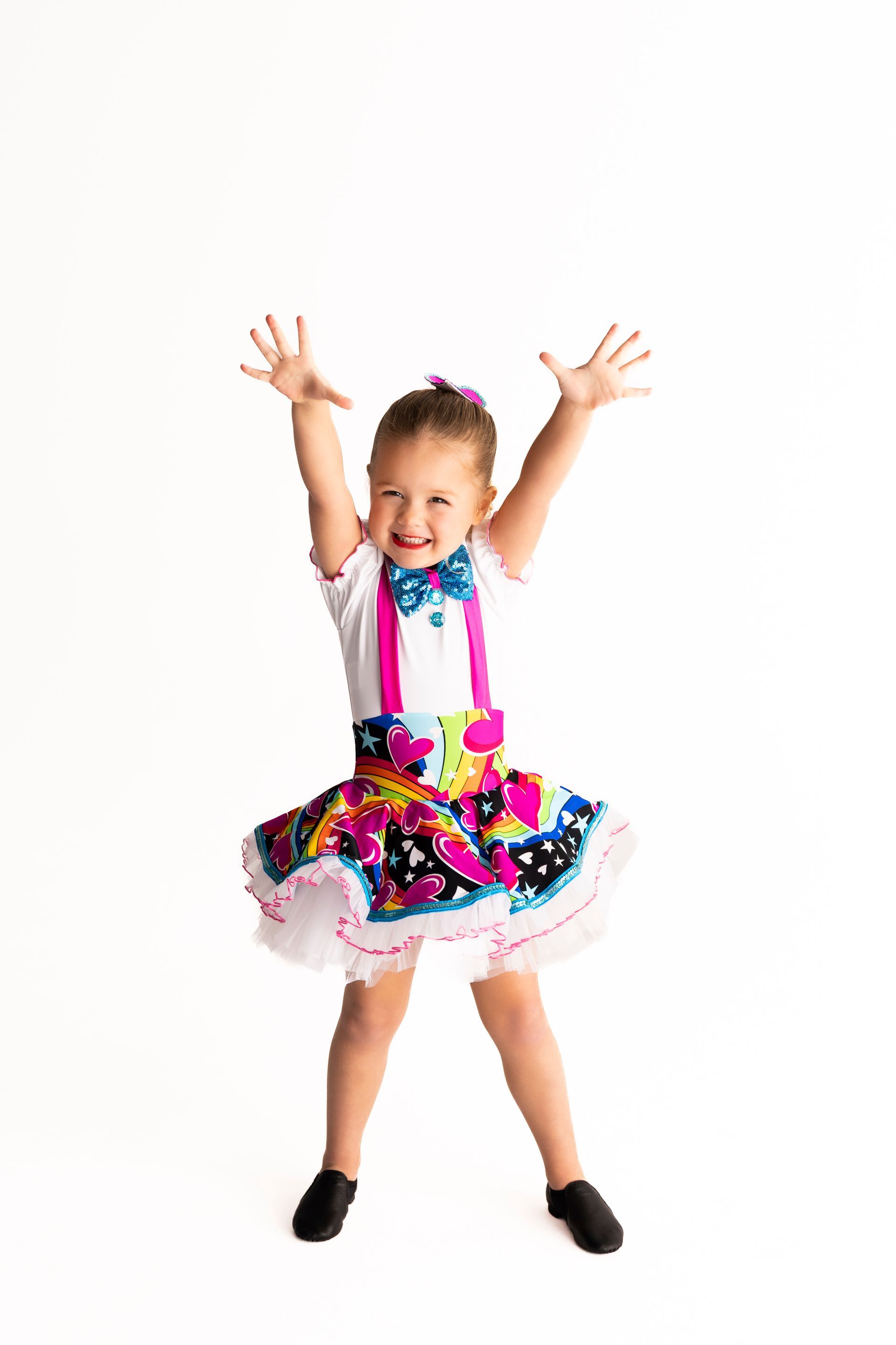 Girl in colorful skirt and suspenders with arms raised and smiling — iDance Performance Co In Medowie, NSW