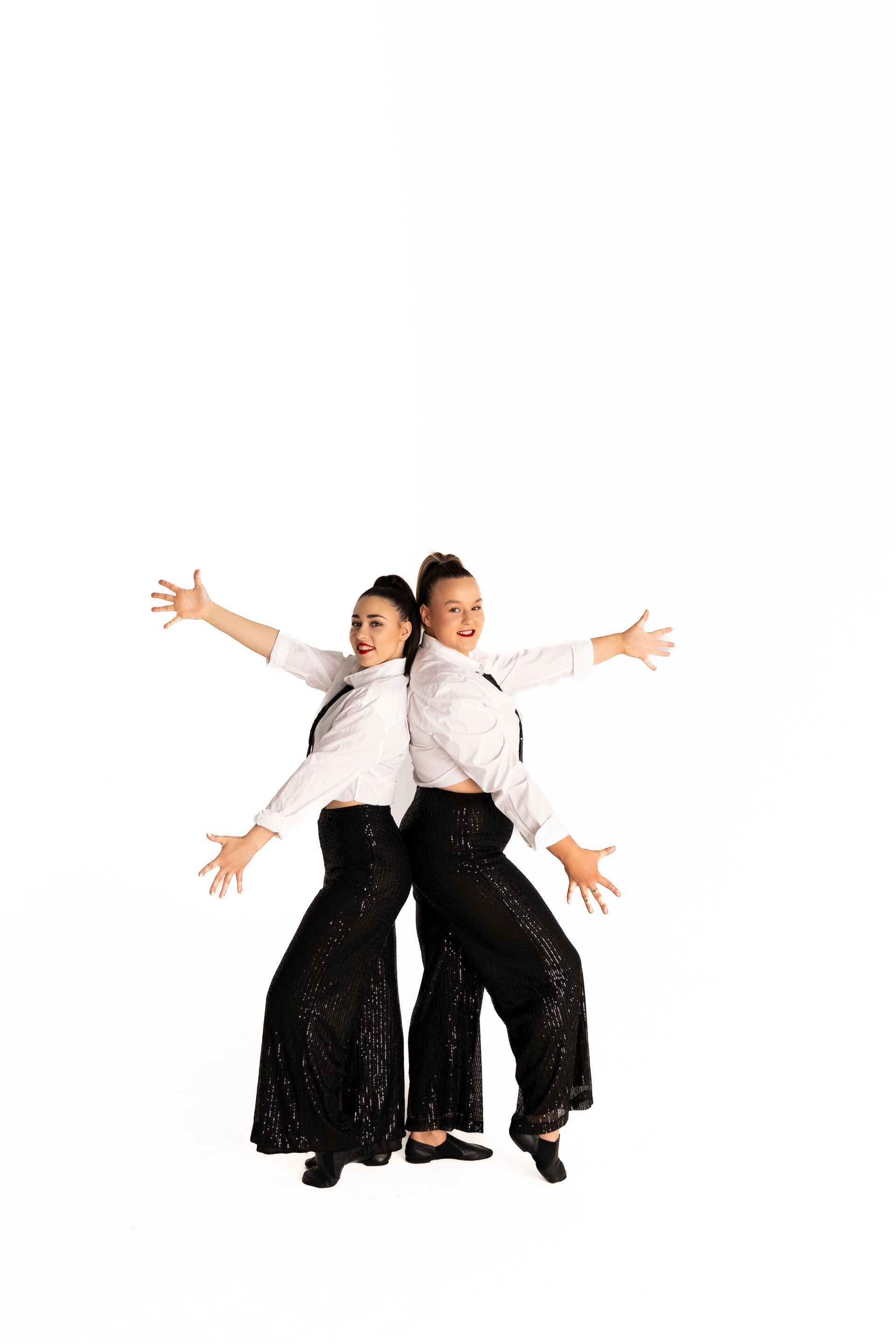 Two people in black sequined pants and white shirts stand back-to-back with arms outstretched — iDance Performance Co In Medowie, NSW