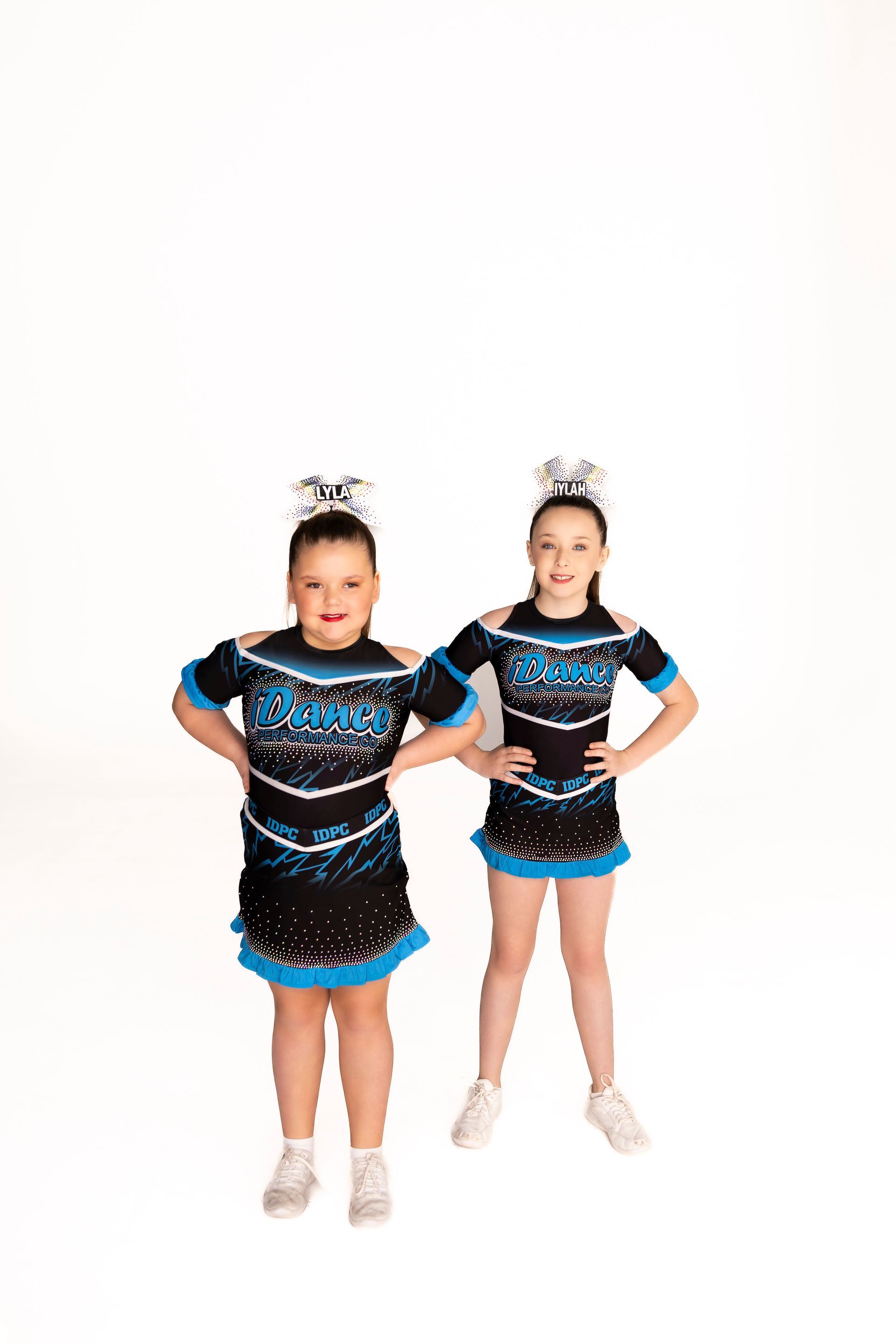 Two cheerleaders in black and teal uniforms with matching headpieces pose in front of a white background — iDance Performance Co In Medowie, NSW