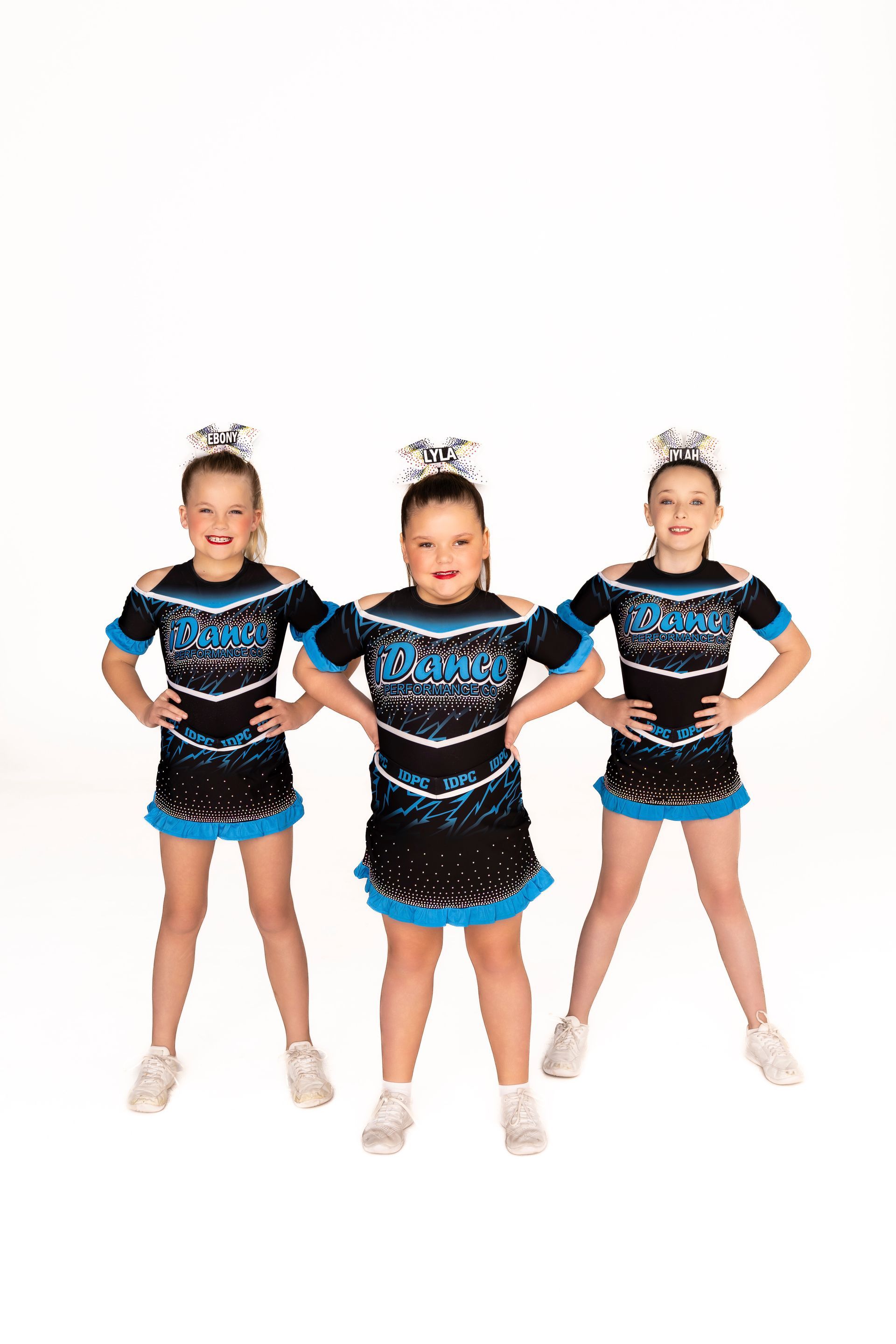 Three cheerleaders in matching blue and black uniforms, hands on hips, smiling, white background — iDance Performance Co In Medowie, NSW