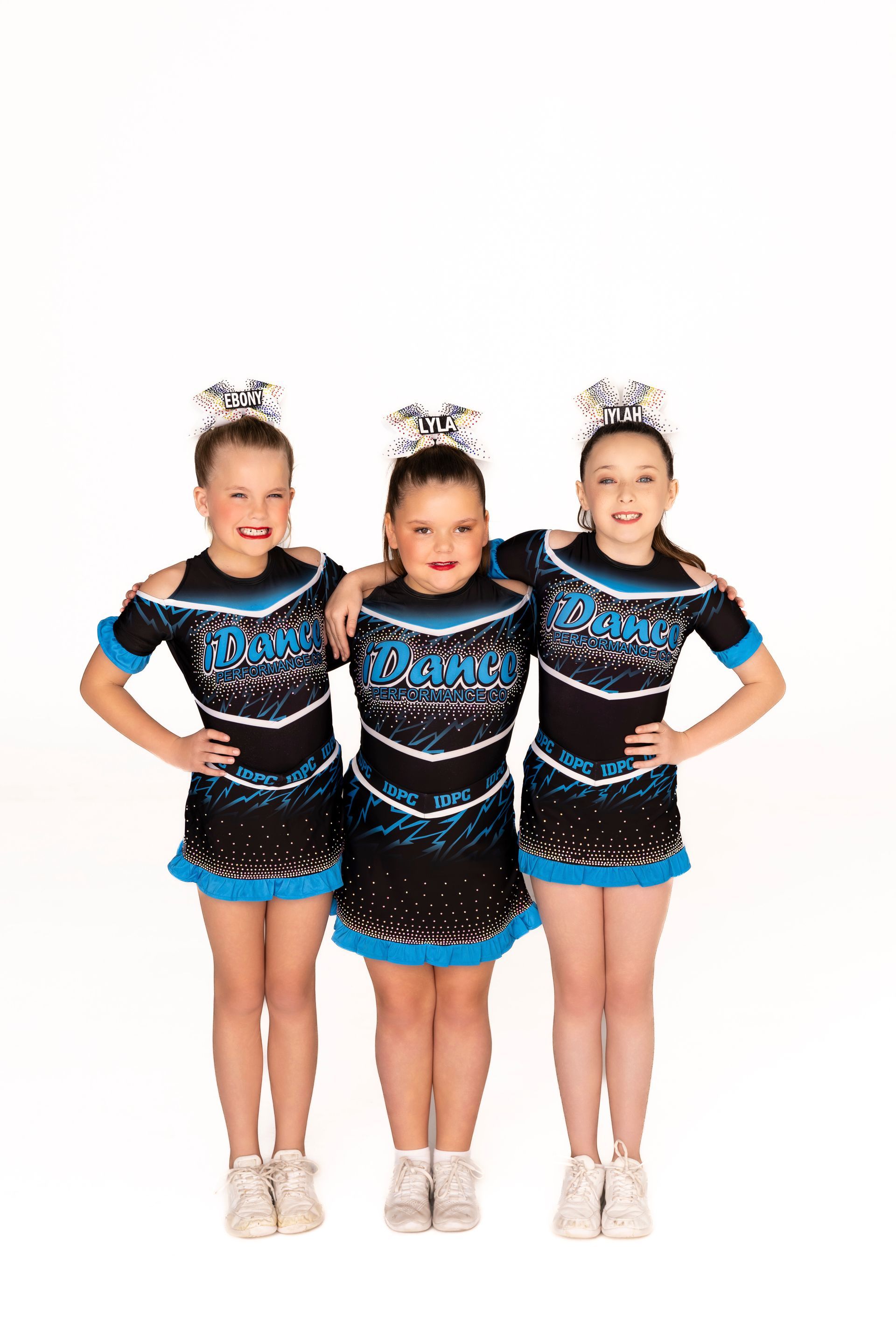 Three cheerleaders in black and blue uniforms pose, arms around each other, on white background — iDance Performance Co In Medowie, NSW