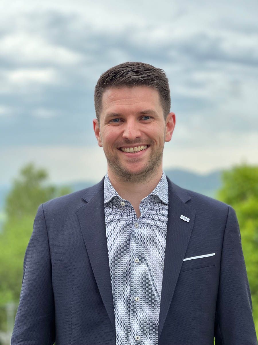 Ein Mann in Anzug und Hemd lächelt in die Kamera.