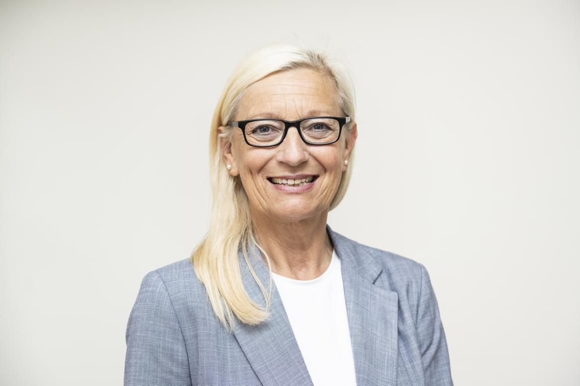 Eine Frau mit Brille und blauer Jacke lächelt in die Kamera.