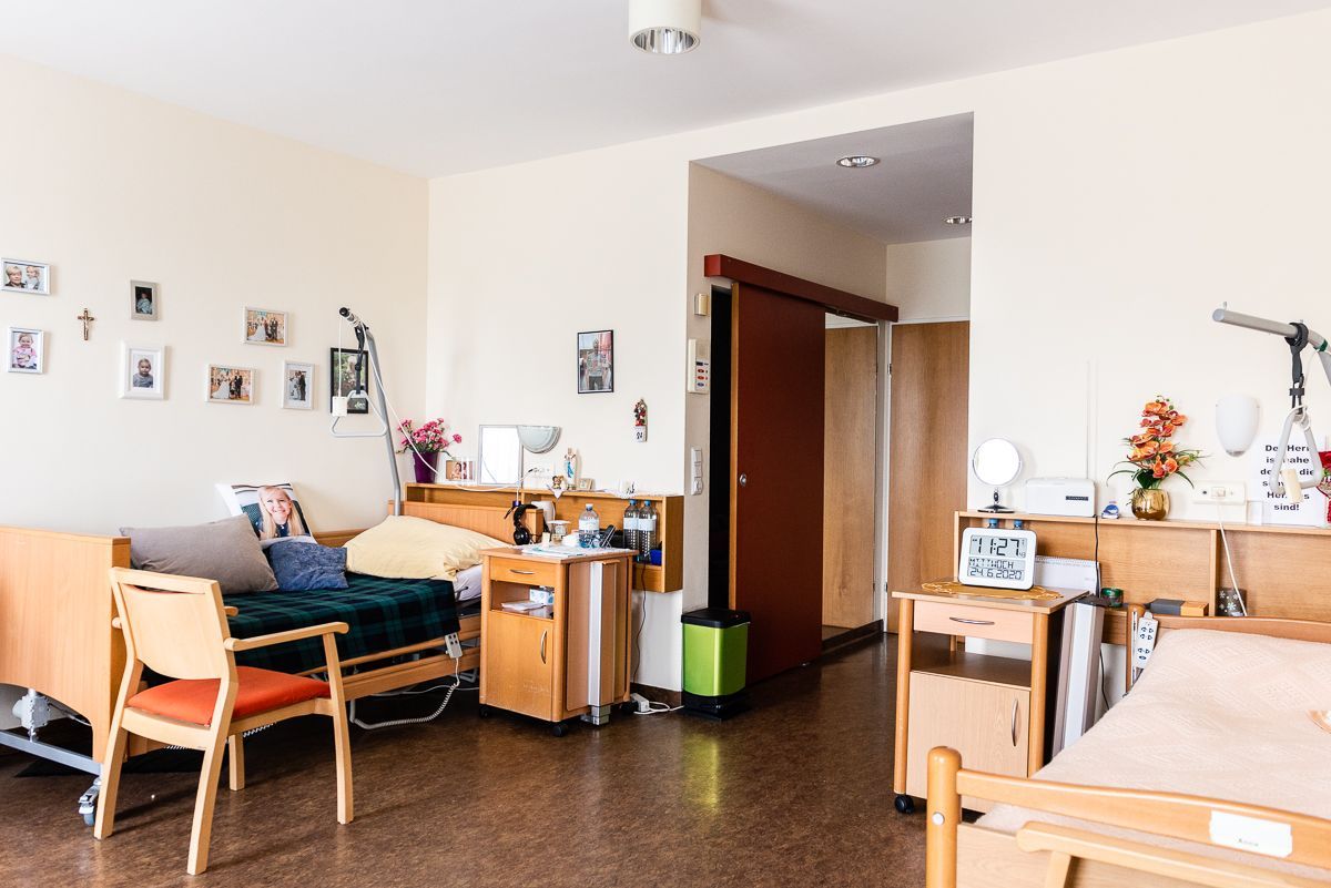 Ein Krankenhauszimmer mit zwei Betten, einem Stuhl und einem Nachttisch.