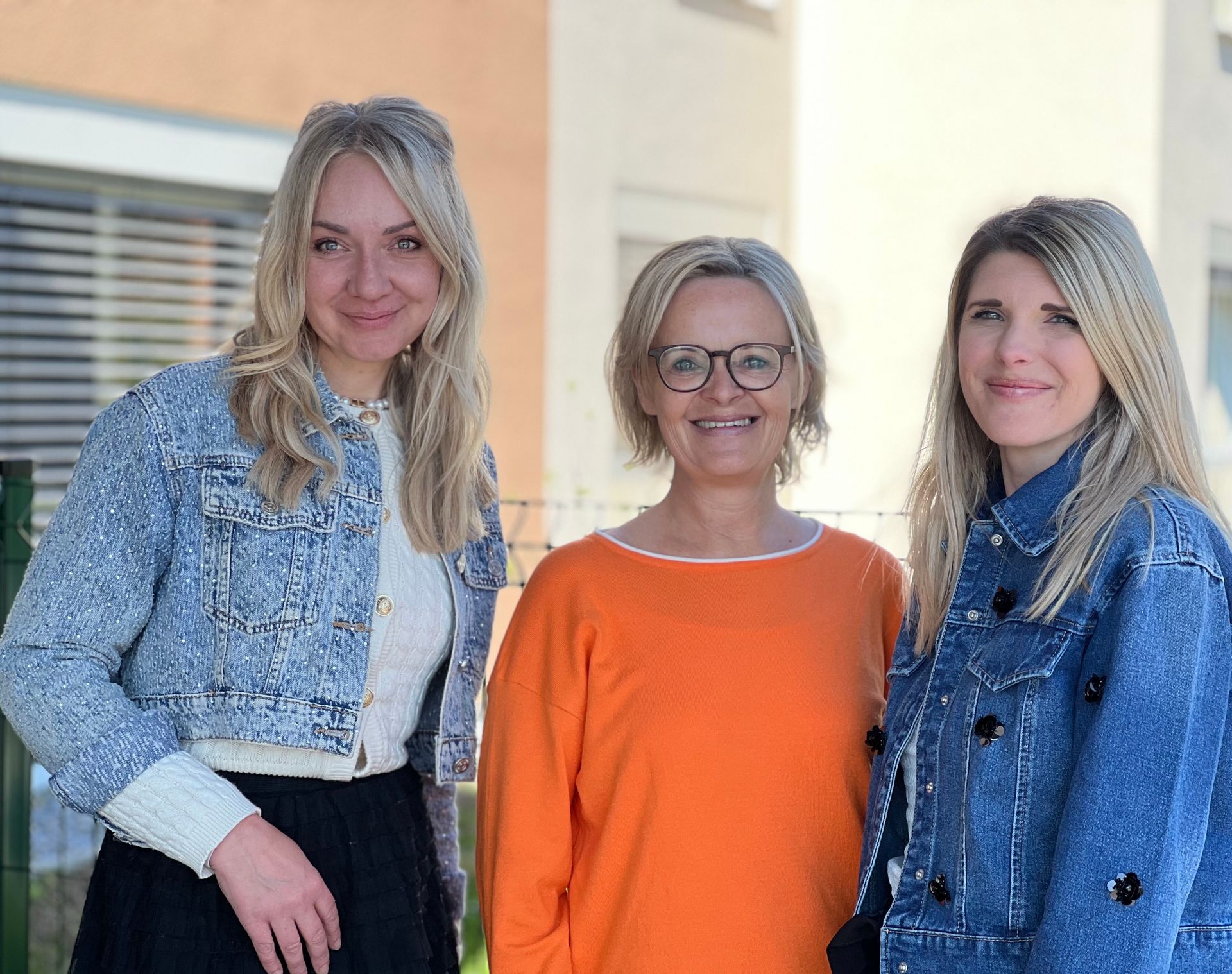 Drei Frauen posieren gemeinsam für ein Foto vor einem Gebäude.