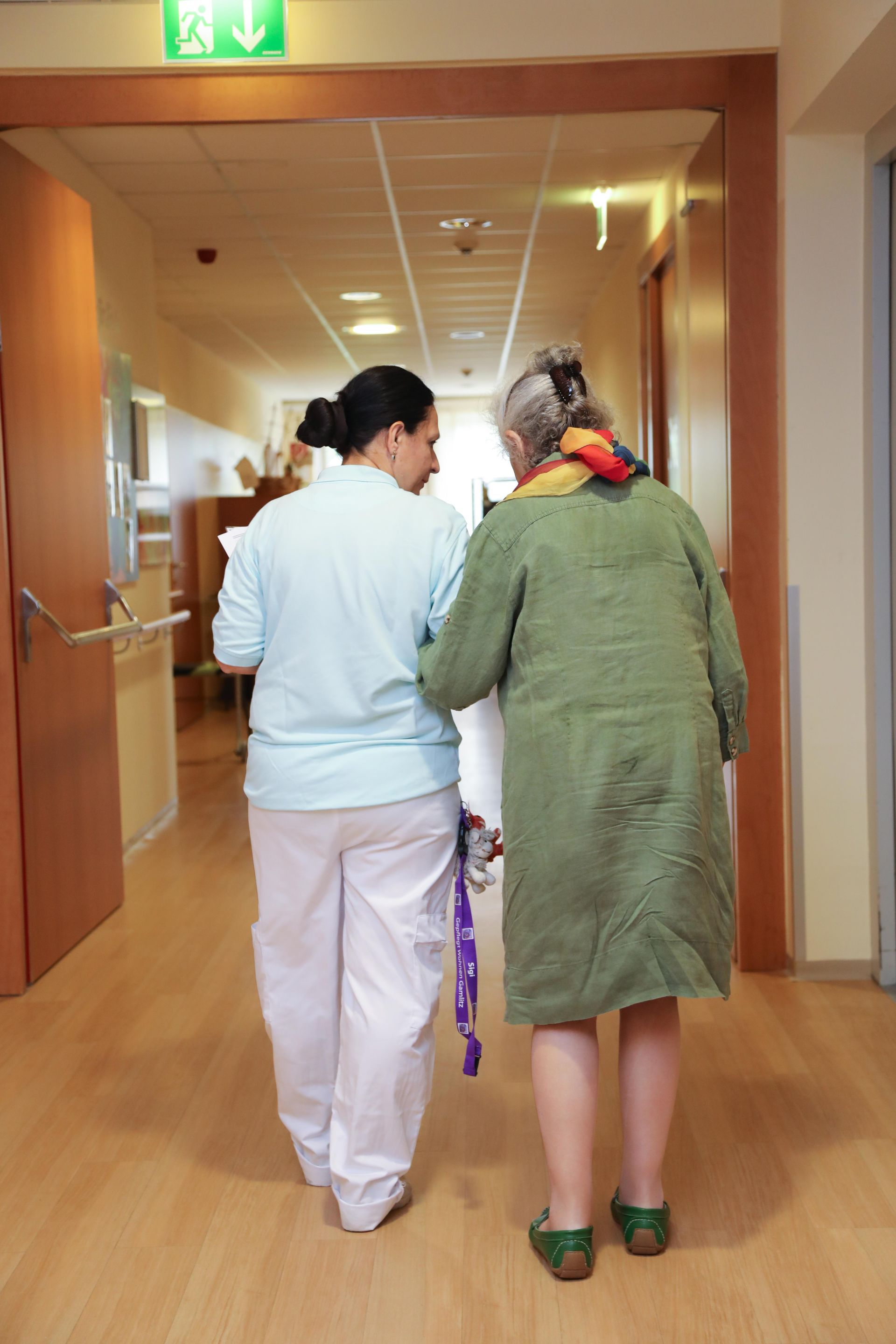 Eine Krankenschwester hilft einer älteren Frau, einen Flur entlang zu gehen.