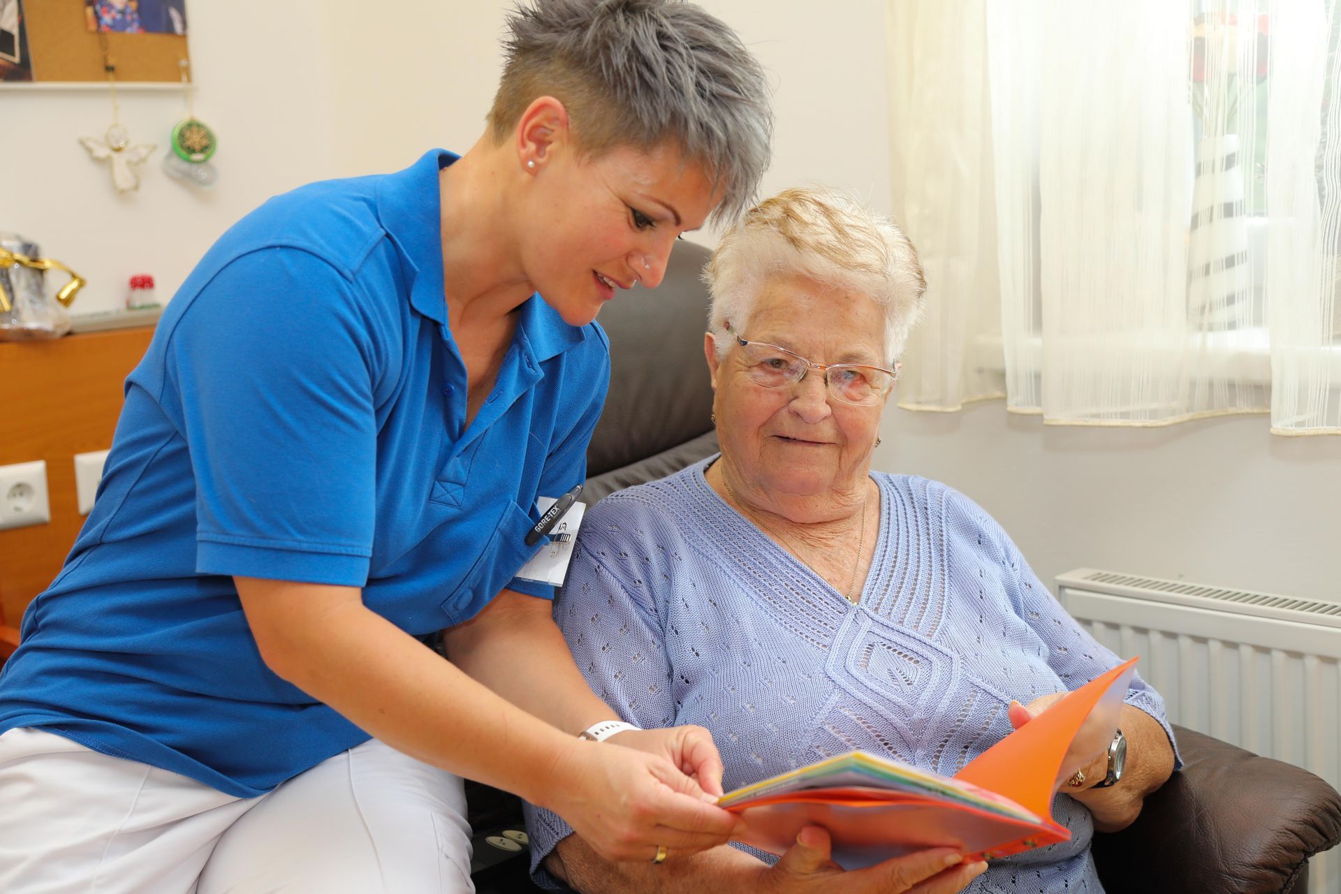 Eine Krankenschwester hilft einer älteren Dame beim Lesen eines Buches.