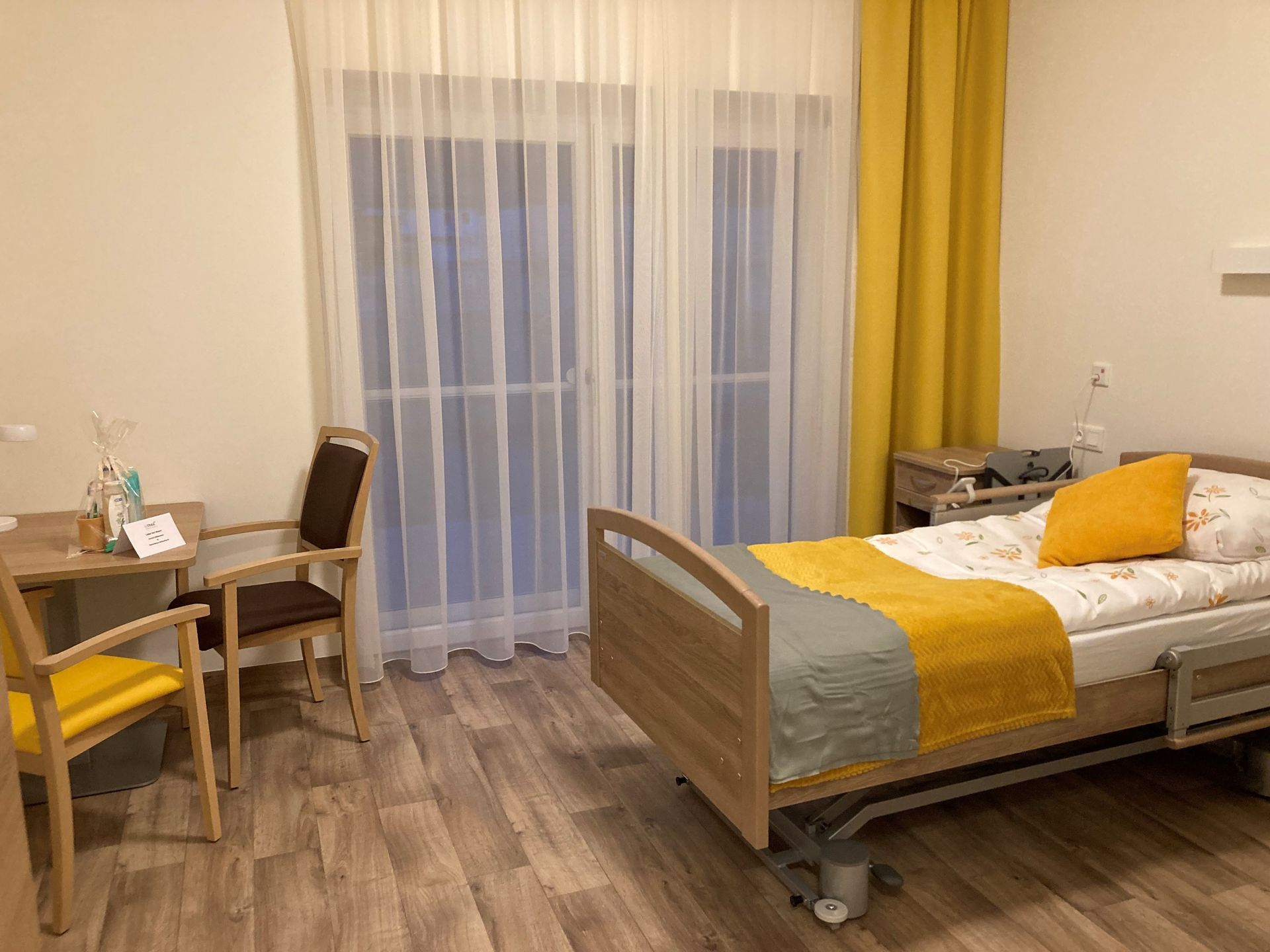 Ein Krankenhauszimmer mit Bett, Tisch, Stühlen und Vorhängen.