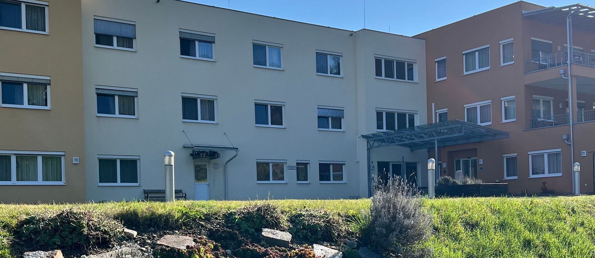 Ein großes Gebäude mit vielen Fenstern ist von Büschen umgeben.