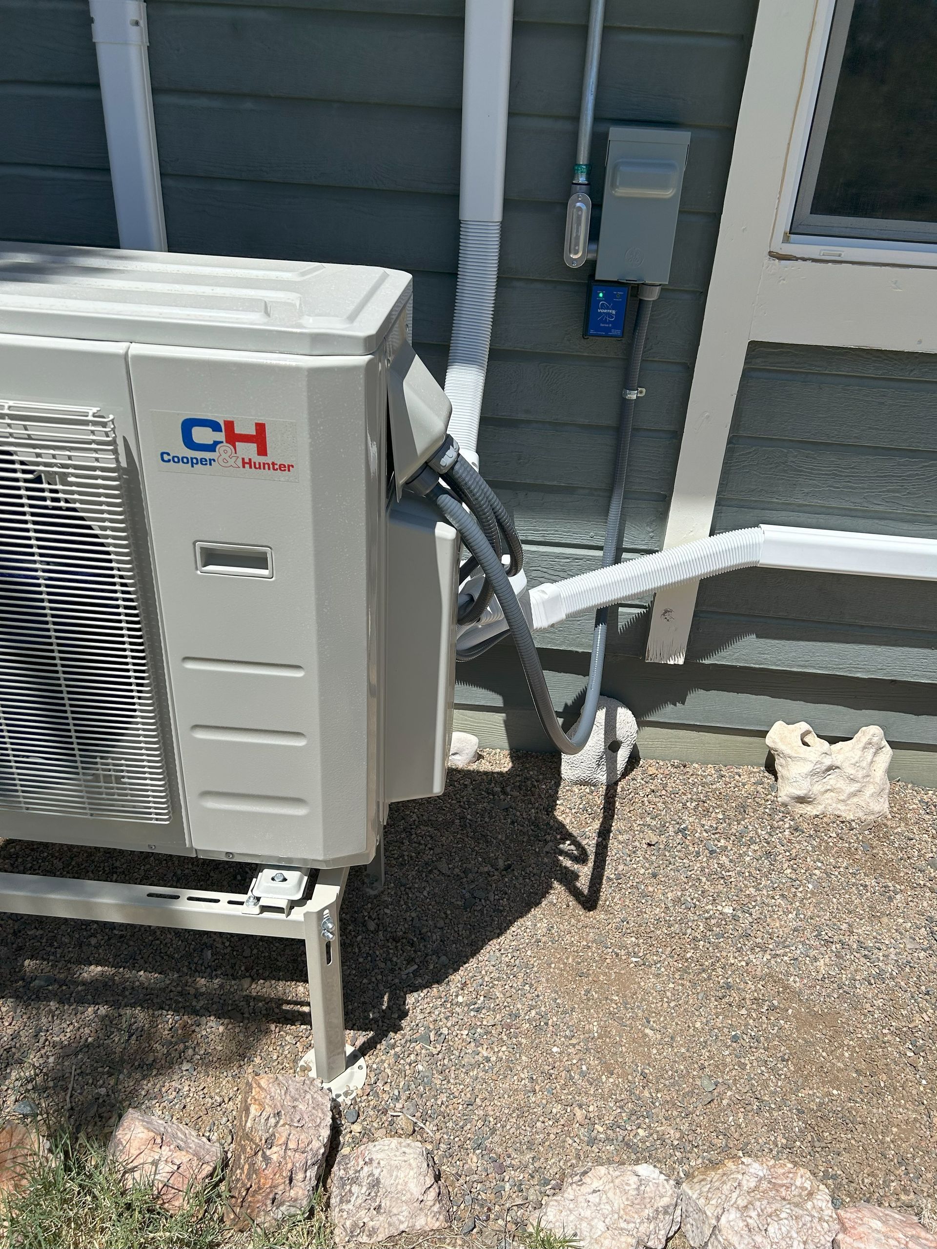 Air conditioning unit outside a blue house, grey pipes and electrical box.