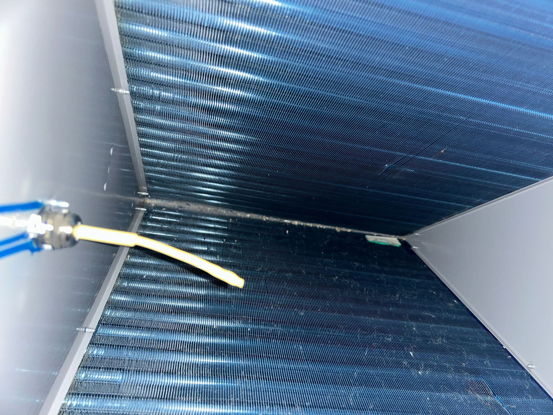 Close-up of air conditioning unit coils with a cleaning tool in use. Blue, silver, and yellow colors.
