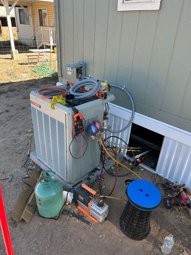 HVAC unit outside a building being serviced with gauges, hoses, and a vacuum pump.