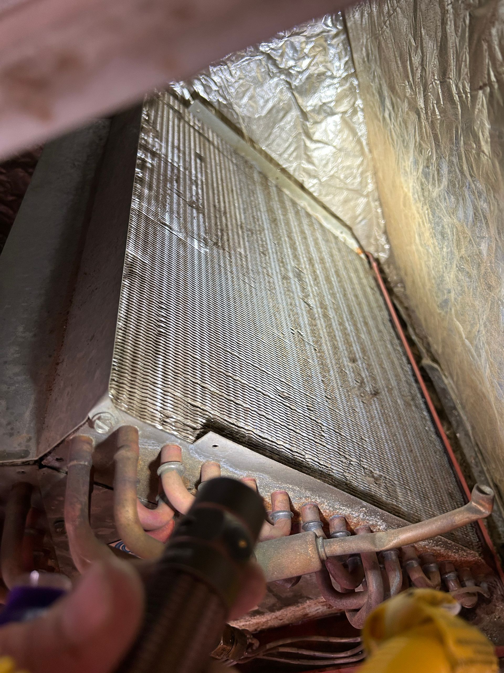Inside an HVAC system, a dirty evaporator coil with copper refrigerant lines.