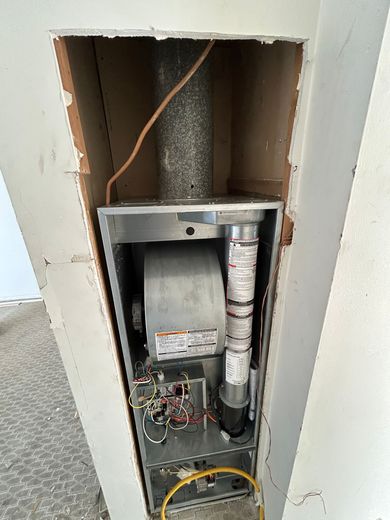 Furnace installed in a wall alcove with exposed wiring and vent pipe.