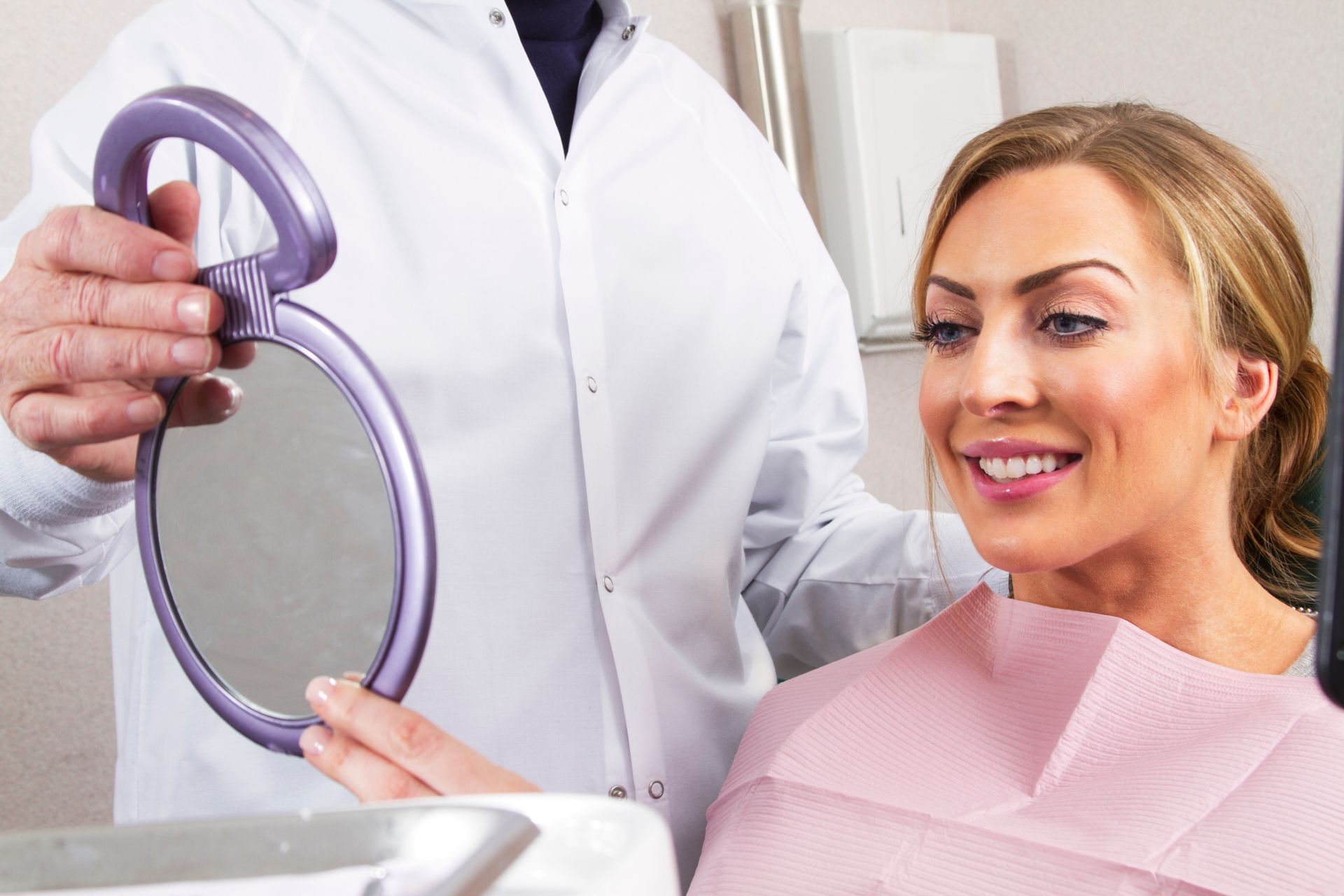 A dentist holds a handheld mirror so his patient can see her smile.