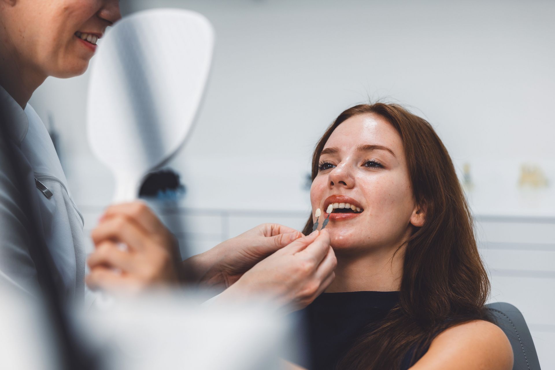 A dental professional is fitting a dental veneer on a smiling patient in a modern dental clinic.