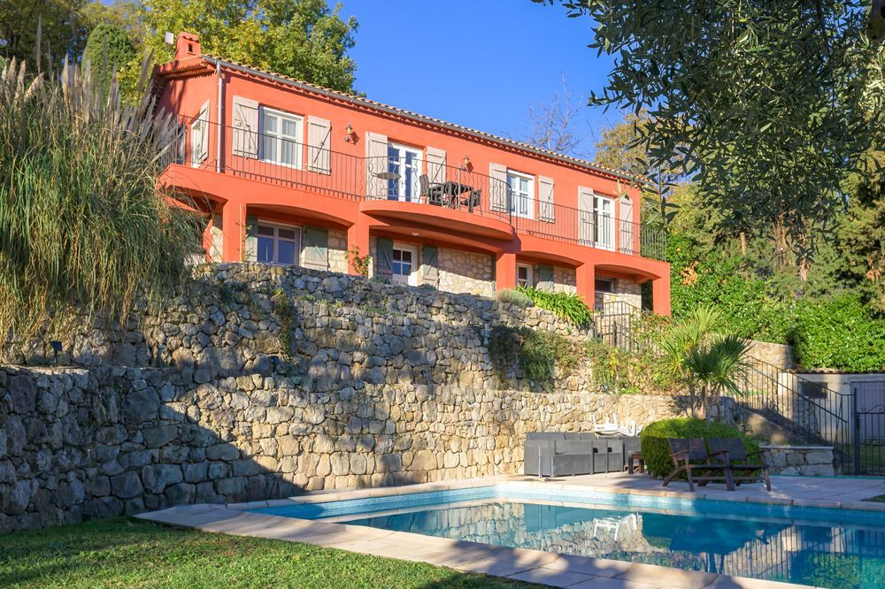 Eingang zu einer geschlossenen Wohnanlage, offene schwarze Metalltore, Straße mit Zebrastreifen, grüne Büsche, blauer Himmel.
