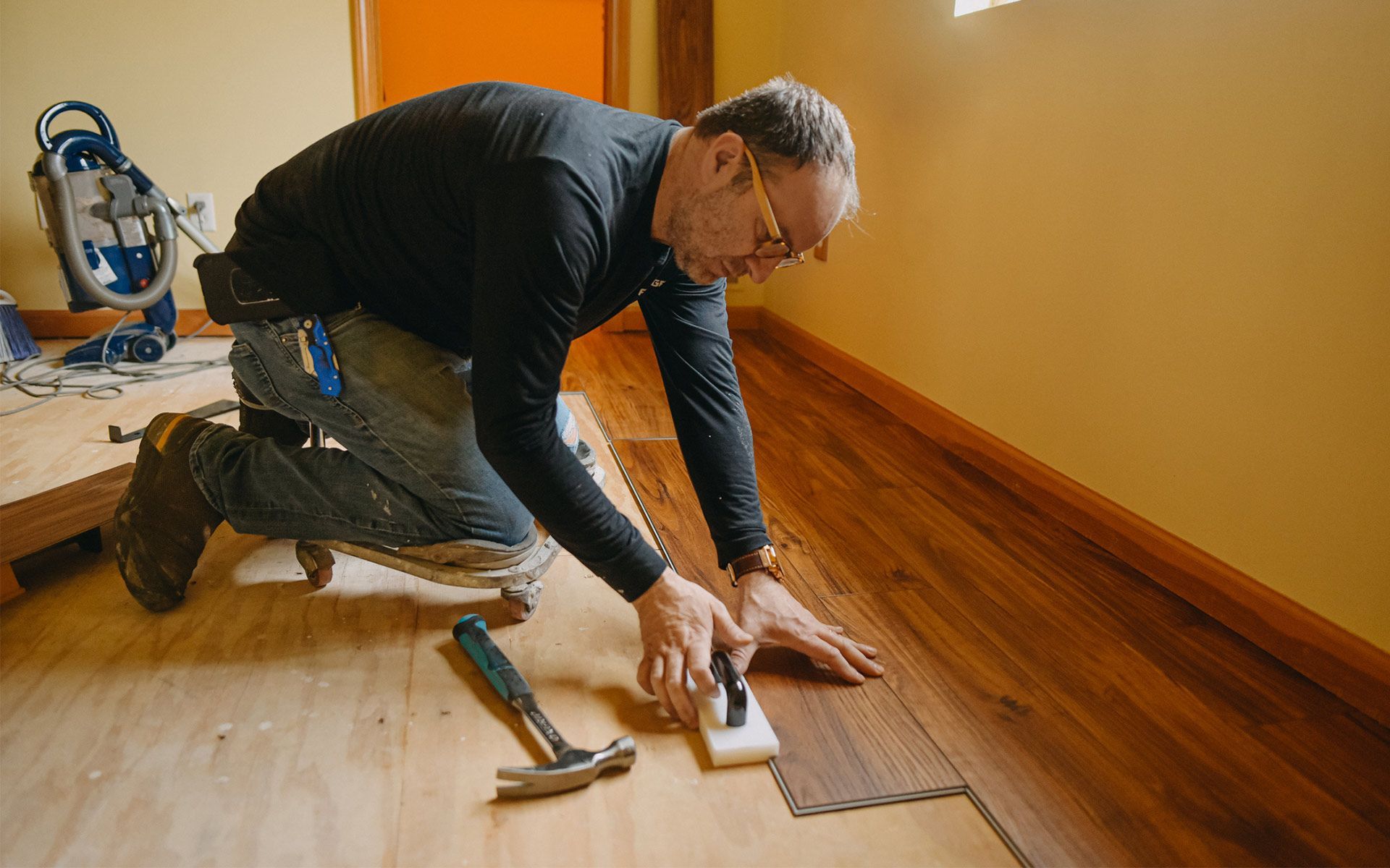 A man is engaged in hardwood flooring installation at home, carefully working on the wooden floor. A man is engaged in hardwood flooring installation at home, carefully working on the wooden floor.