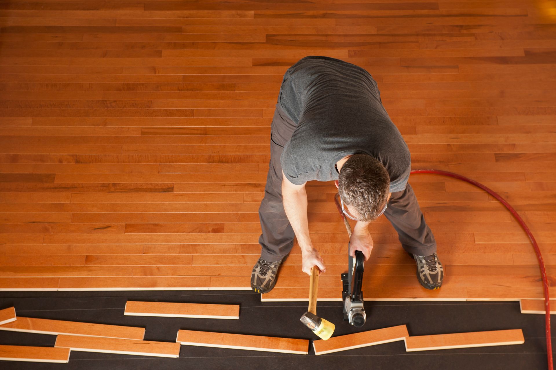 Hardwood planks are being installed as a worker uses a mallet and a flooring nailer.