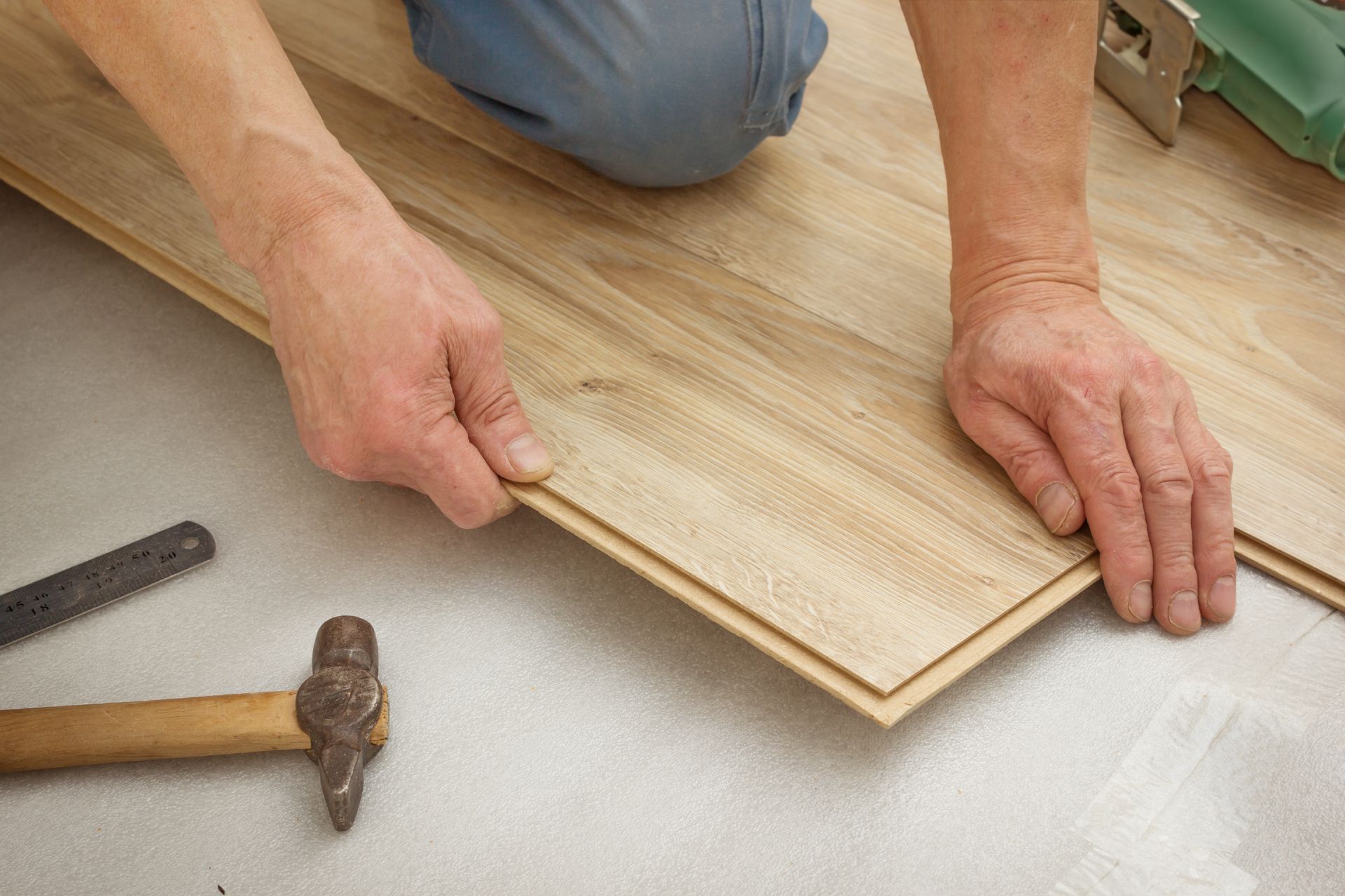 A man is engaged in hardwood flooring replacement at home, carefully working on the wooden floor.