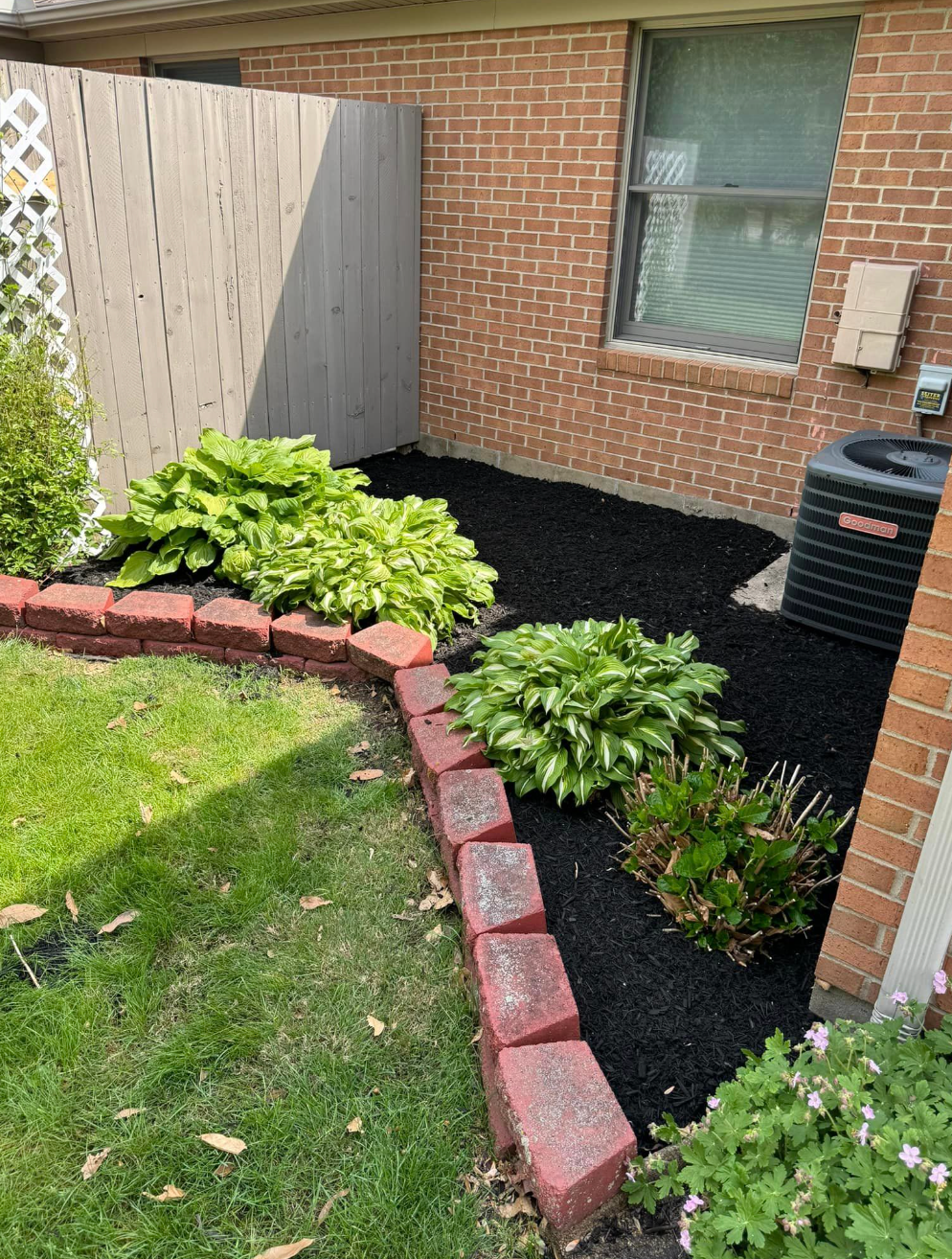 A brick house with a fence and a black mulch garden in front of it.
