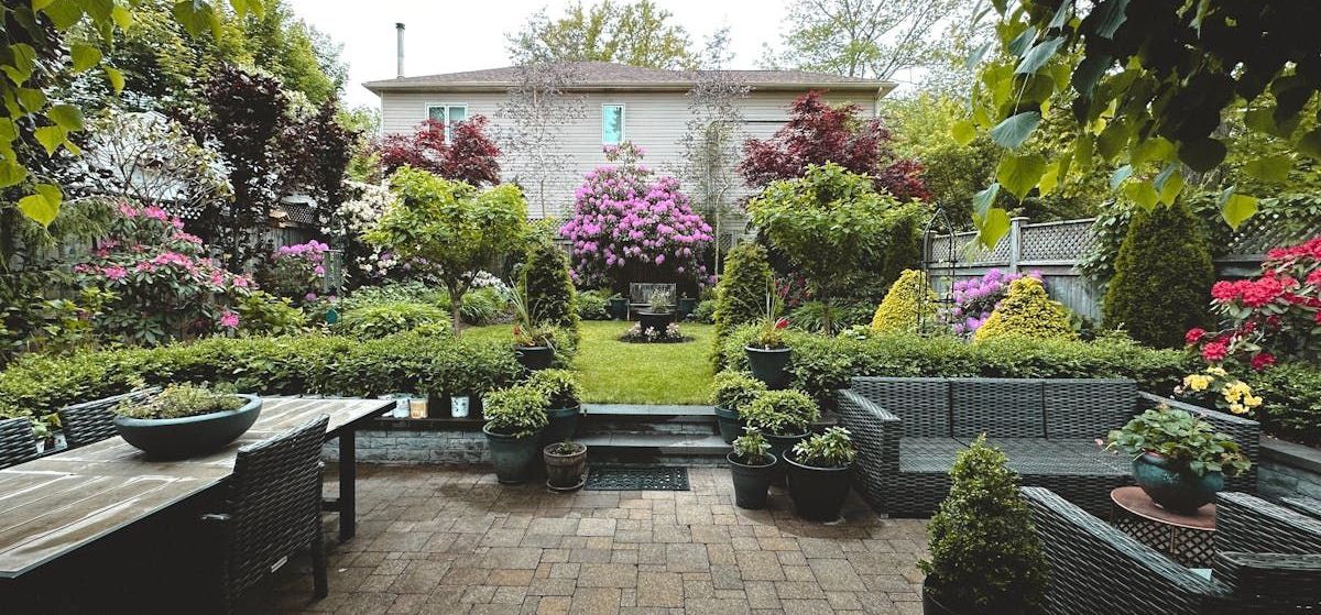 A patio with a table and chairs in a garden with a house in the background.
