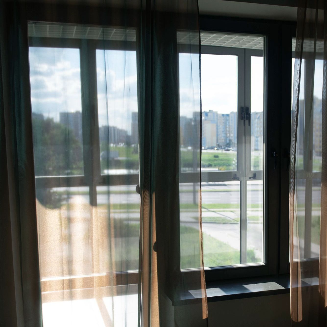 A window with sheer curtains and a view of a city