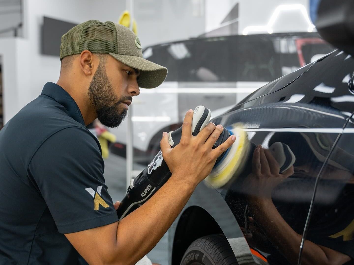 A man is polishing a red car with a polisher.