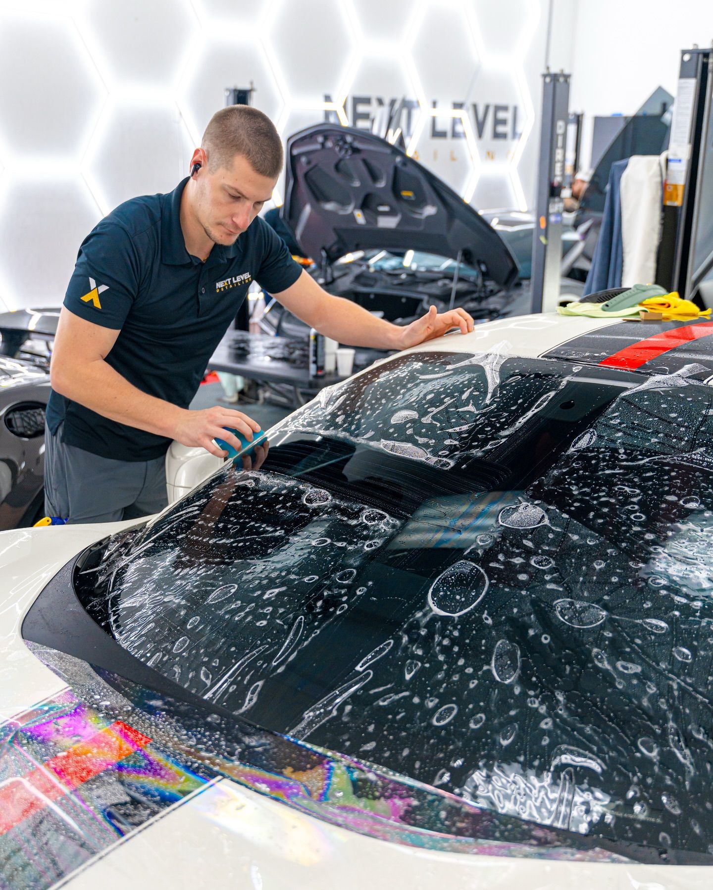 Man applying film to a car's windshield. He's in a shop with 