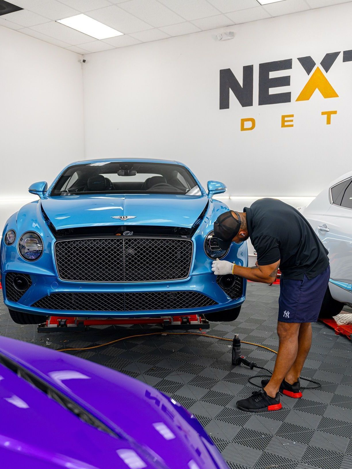 A man is cleaning the hood of a black car in a garage.