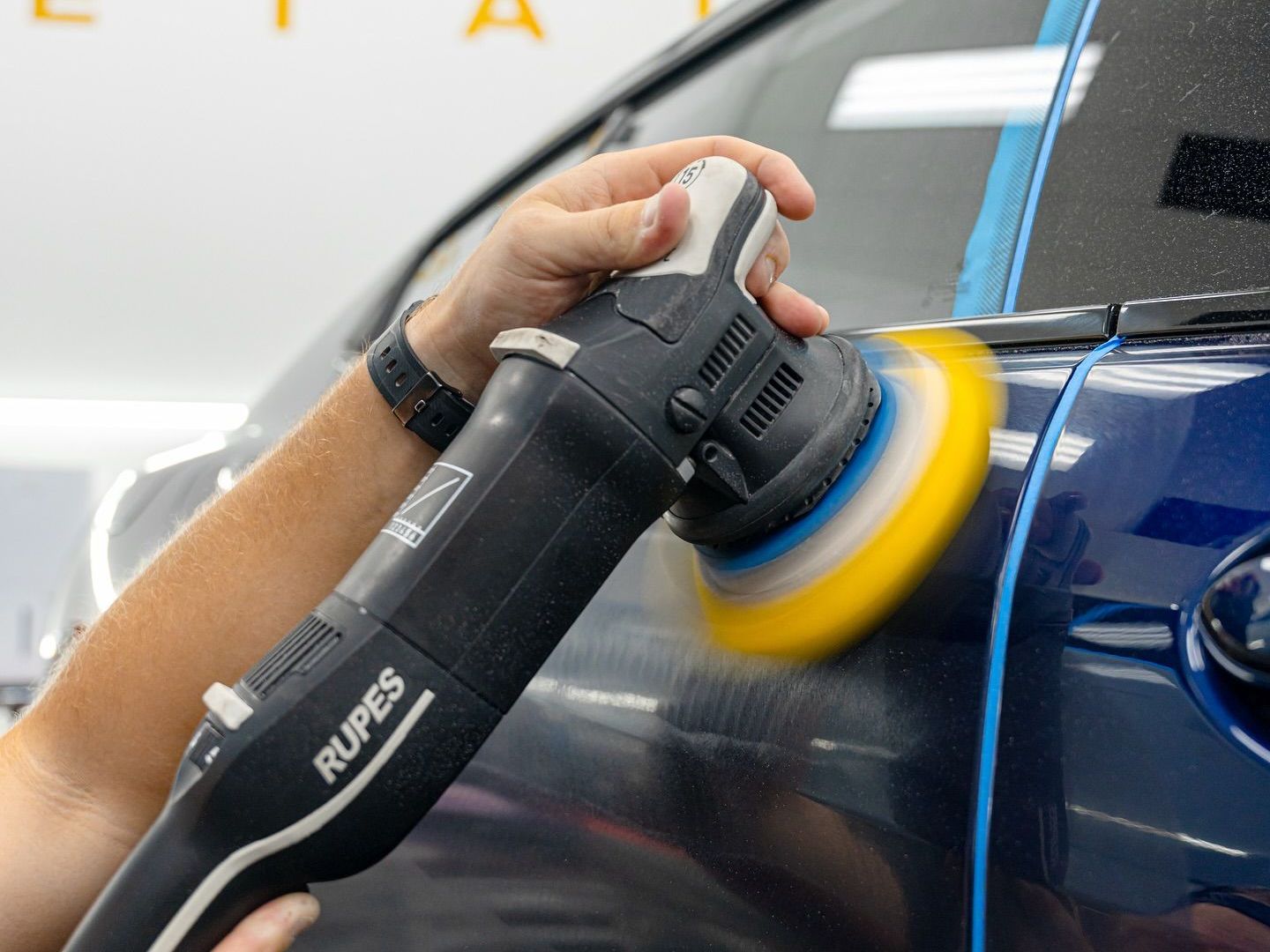 A person is polishing a red car with a machine.
