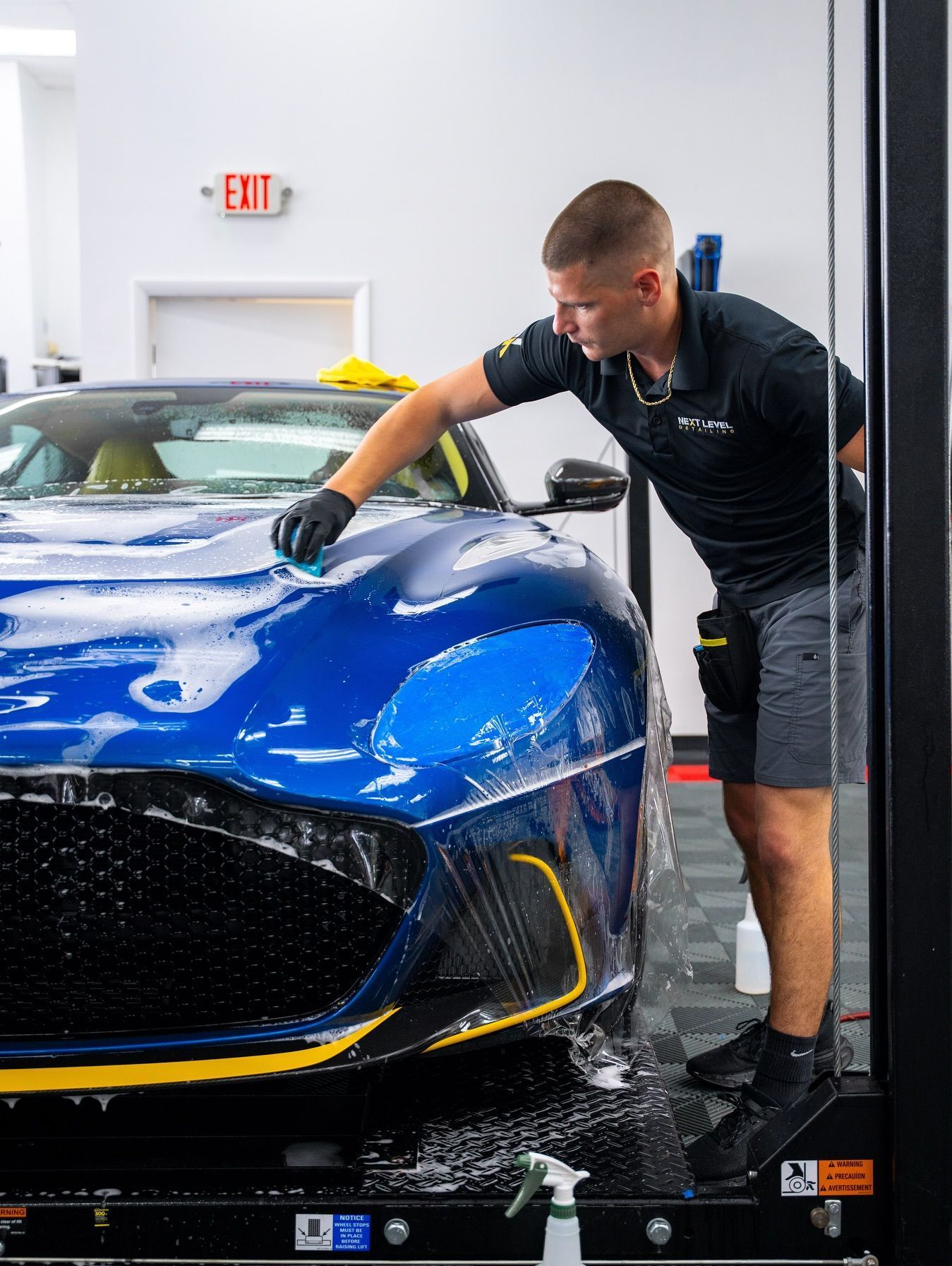 A man is wrapping a blue car with plastic